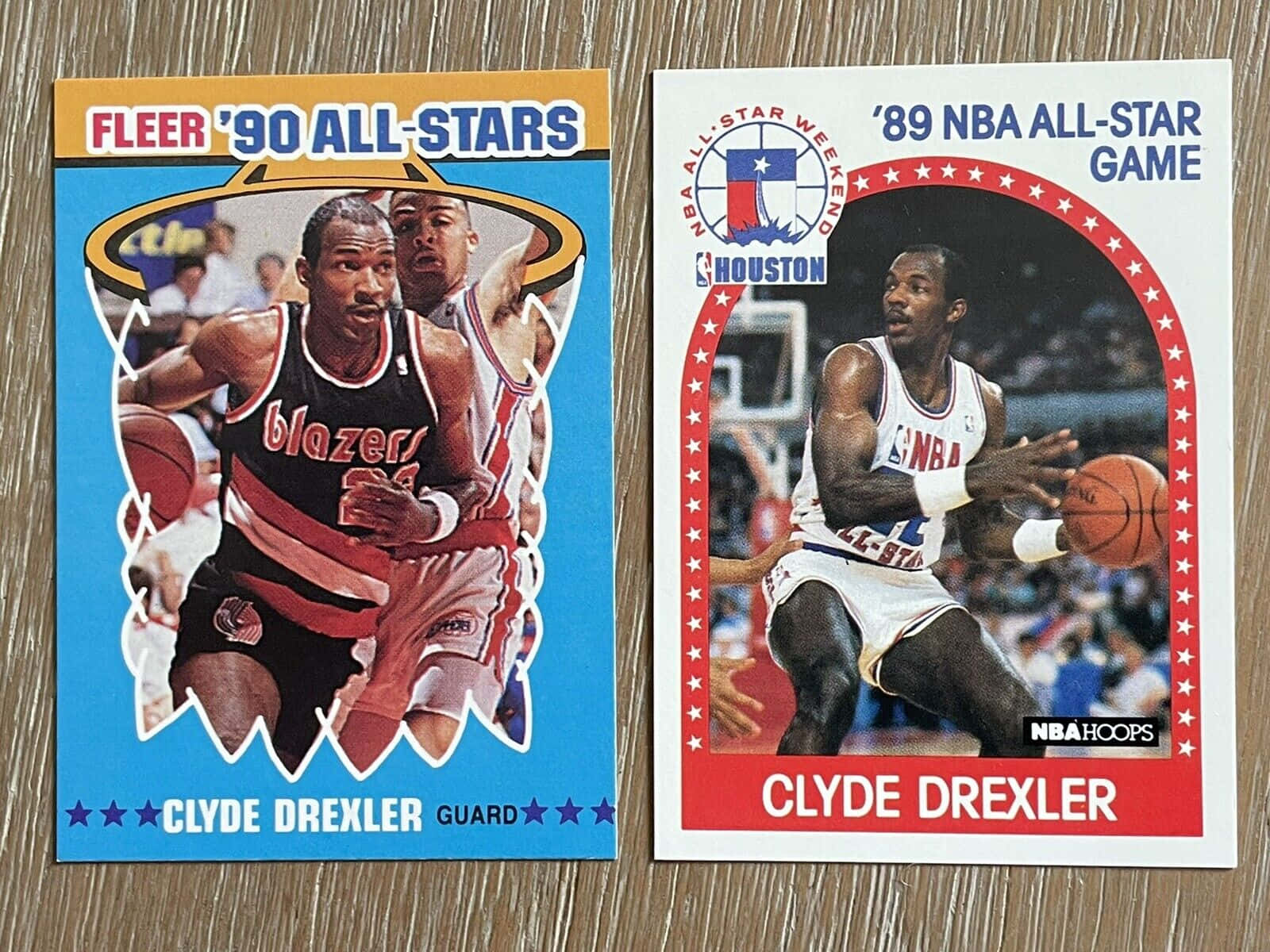 克萊德·德雷克斯勒 1980-1990年代 NBA 全明星賽照片卡 壁紙 — 兩張 Clyde Drexler 的復古 NBA 全明星交換卡並排放在木質表面上。