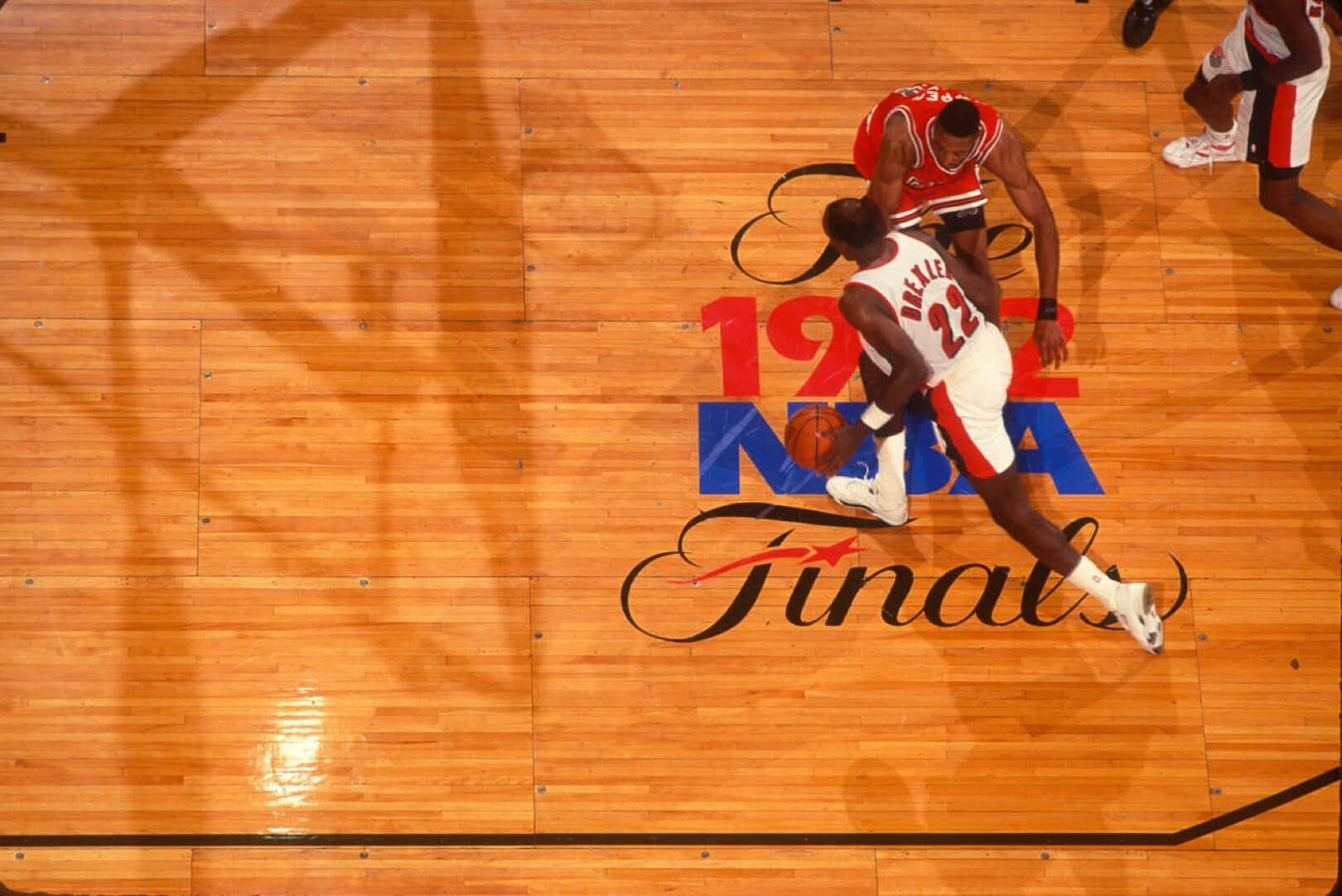 克萊德·德雷克斯勒1992年NBA總決賽空中攝影 壁紙 — 從上方俯瞰一名籃球運動員在帶有1992年NBA總決賽標誌的硬木球場上運球越過防守球員。
