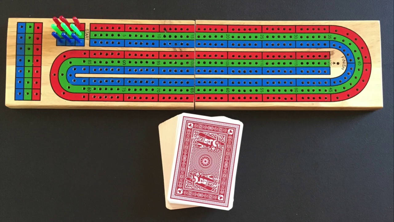 深色桌子上放著木製克里比奇棋盤、棋子和一副撲克牌。