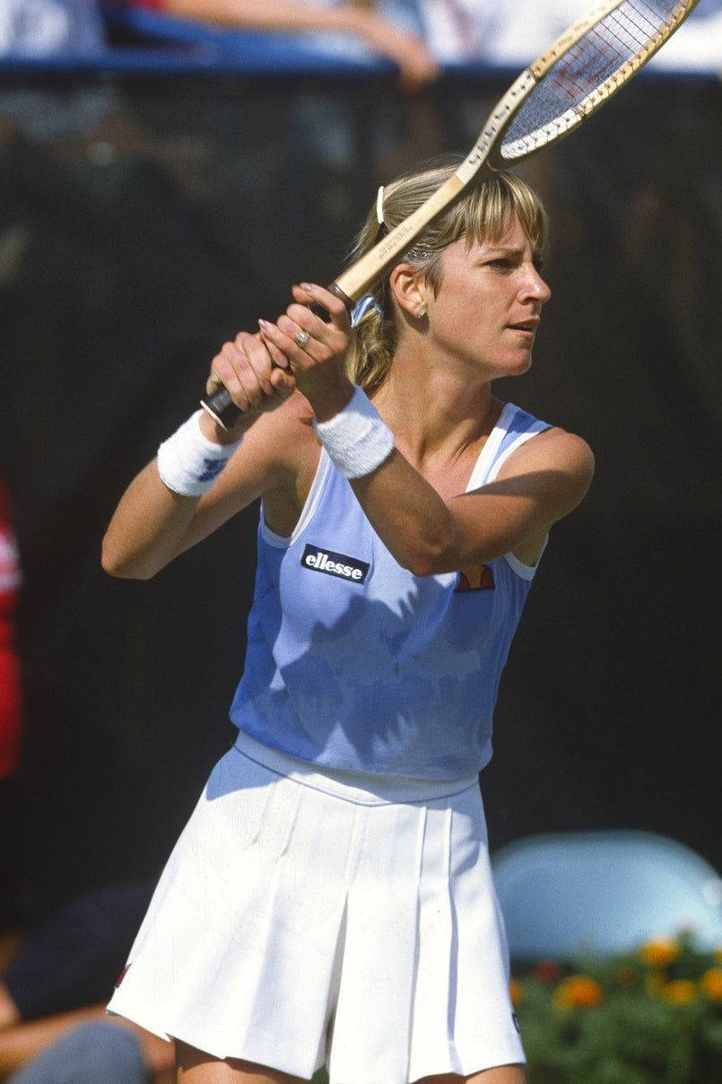 女網球運動員揮拍中，身穿藍色上衣和白色裙子