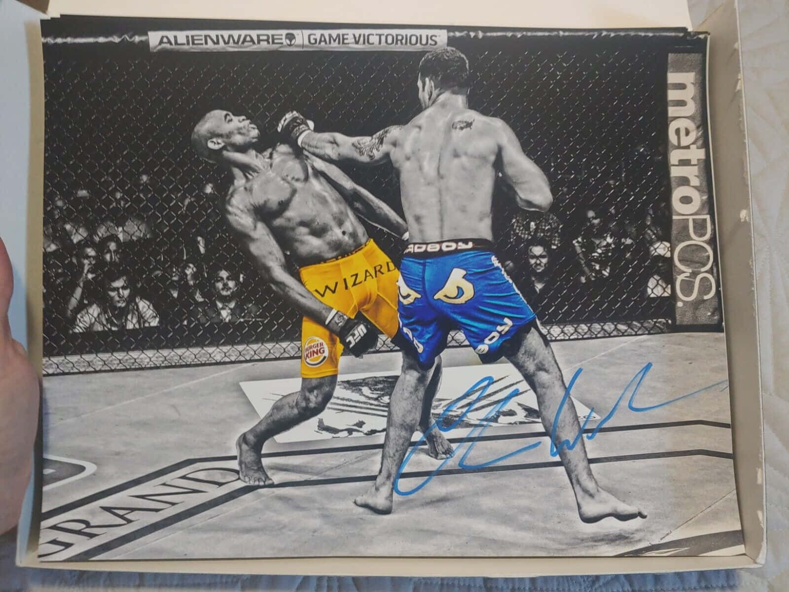 兩名MMA拳手在籠中比賽，一人踢向另一人的簽名照片。