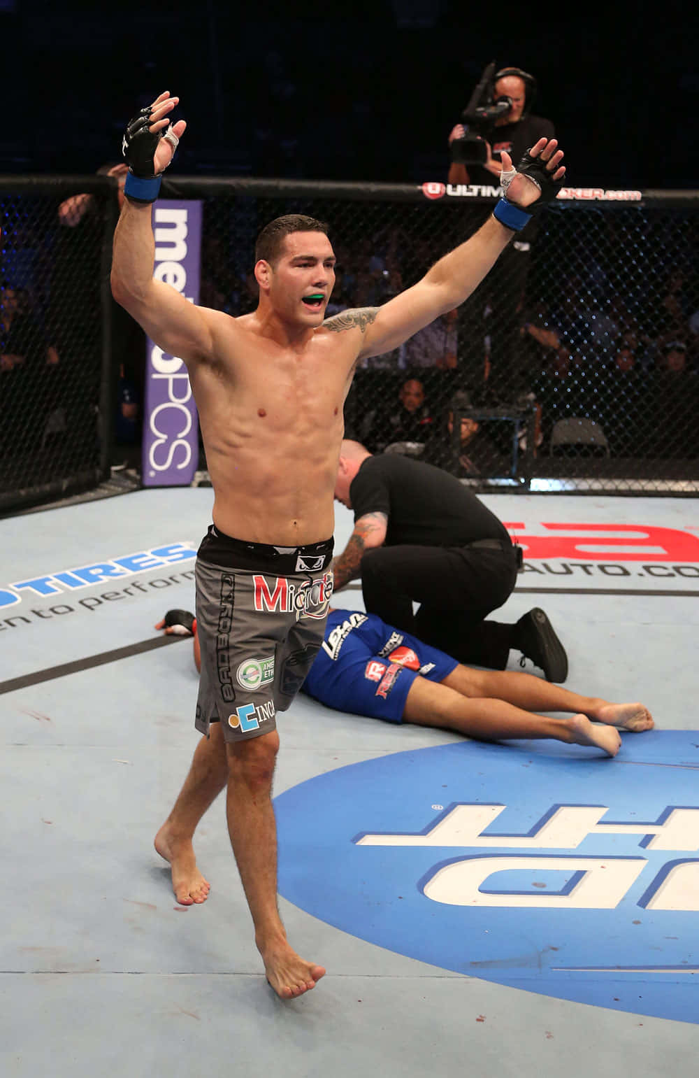 MMA拳手在八角籠中慶祝擊敗倒下的對手。