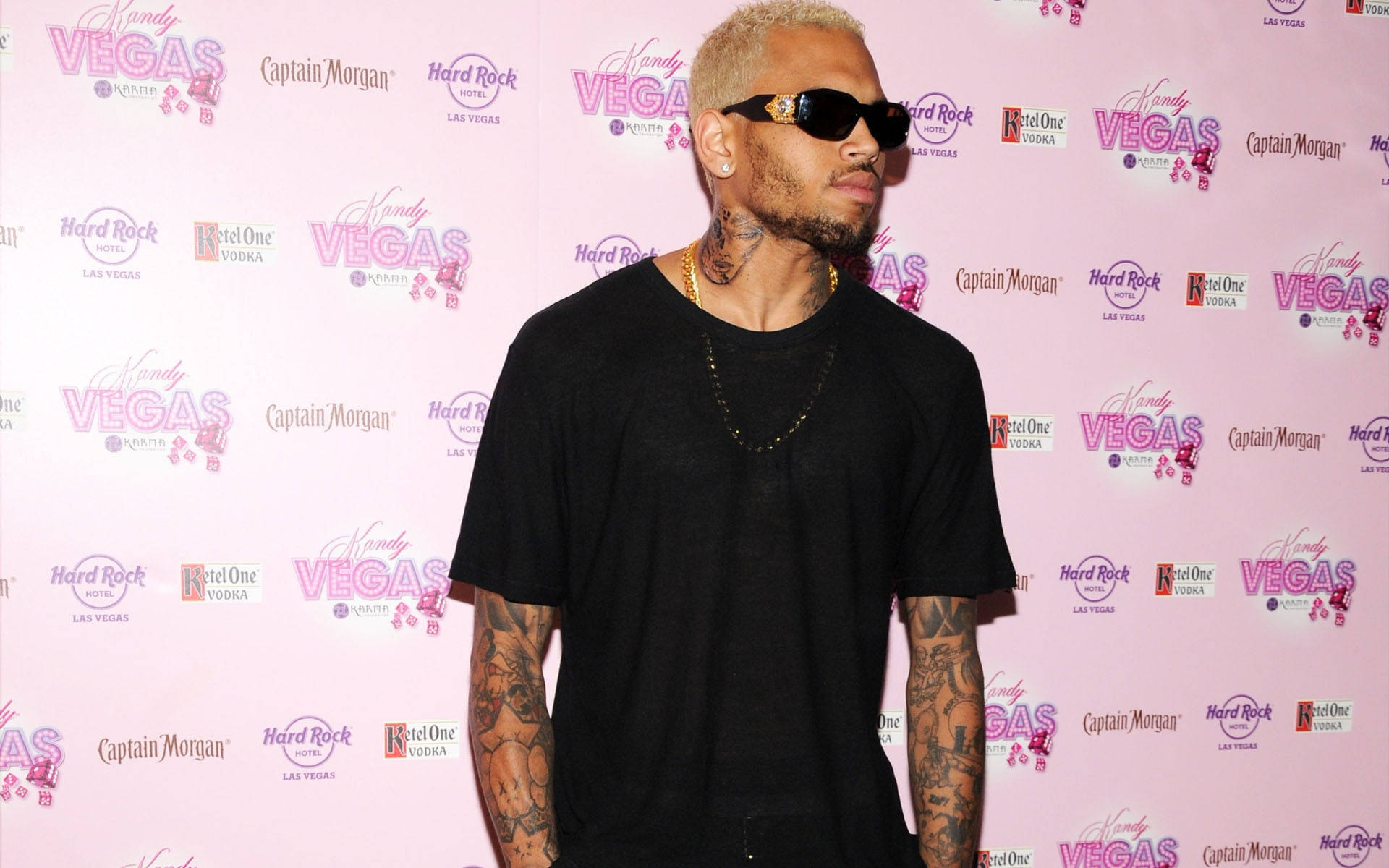 克里斯·布朗 凱迪維加斯勞動節 壁紙 — Chris Brown 自信地穿著黑色服裝和太陽眼鏡，在粉紅色的品牌活動背景前擺姿勢。