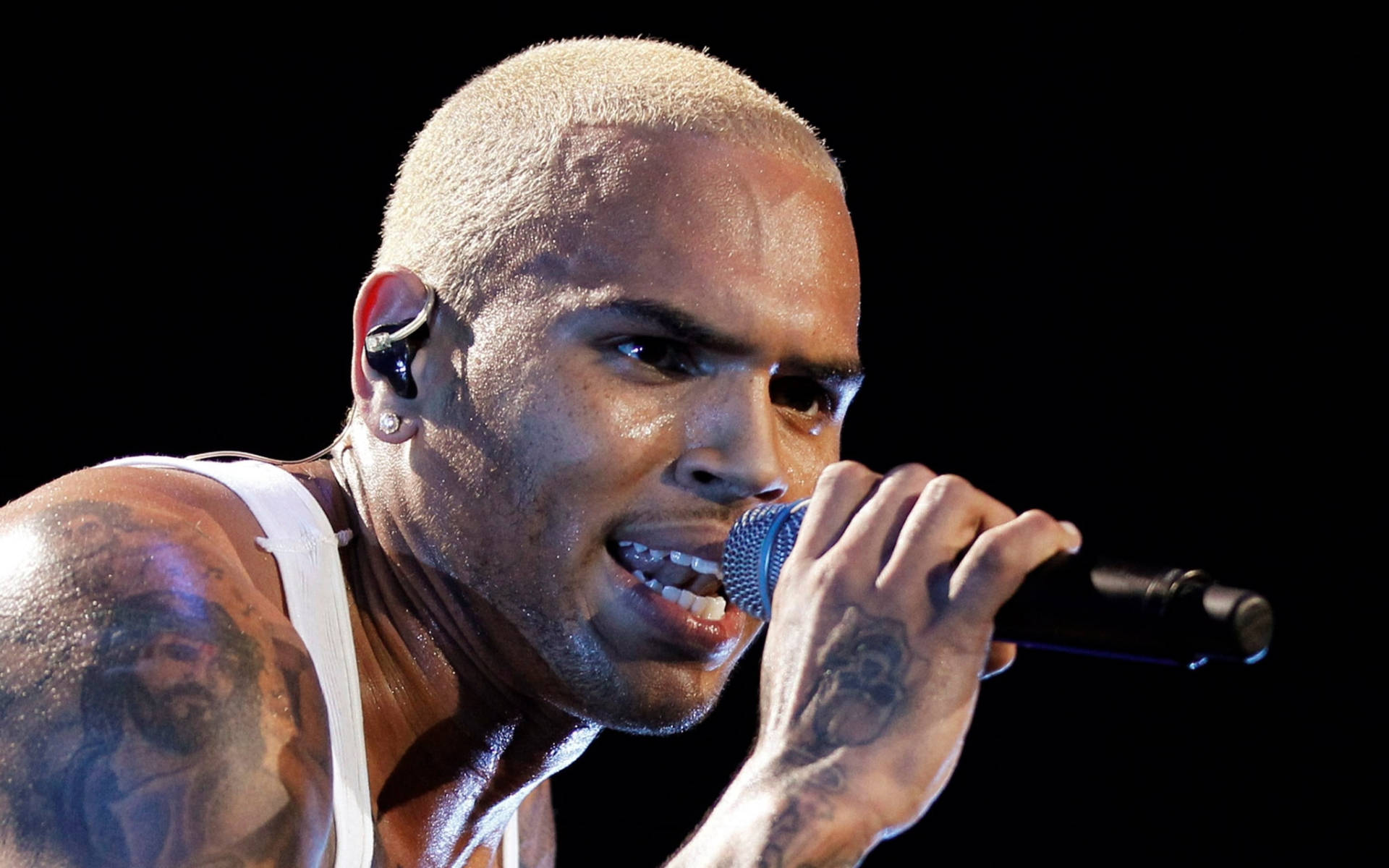 克里斯·布朗 近距離攝影 壁紙 — 一位滿頭大汗、剃光頭、有紋身的男歌手，在黑色背景前熱情地對著咪高峰演唱。