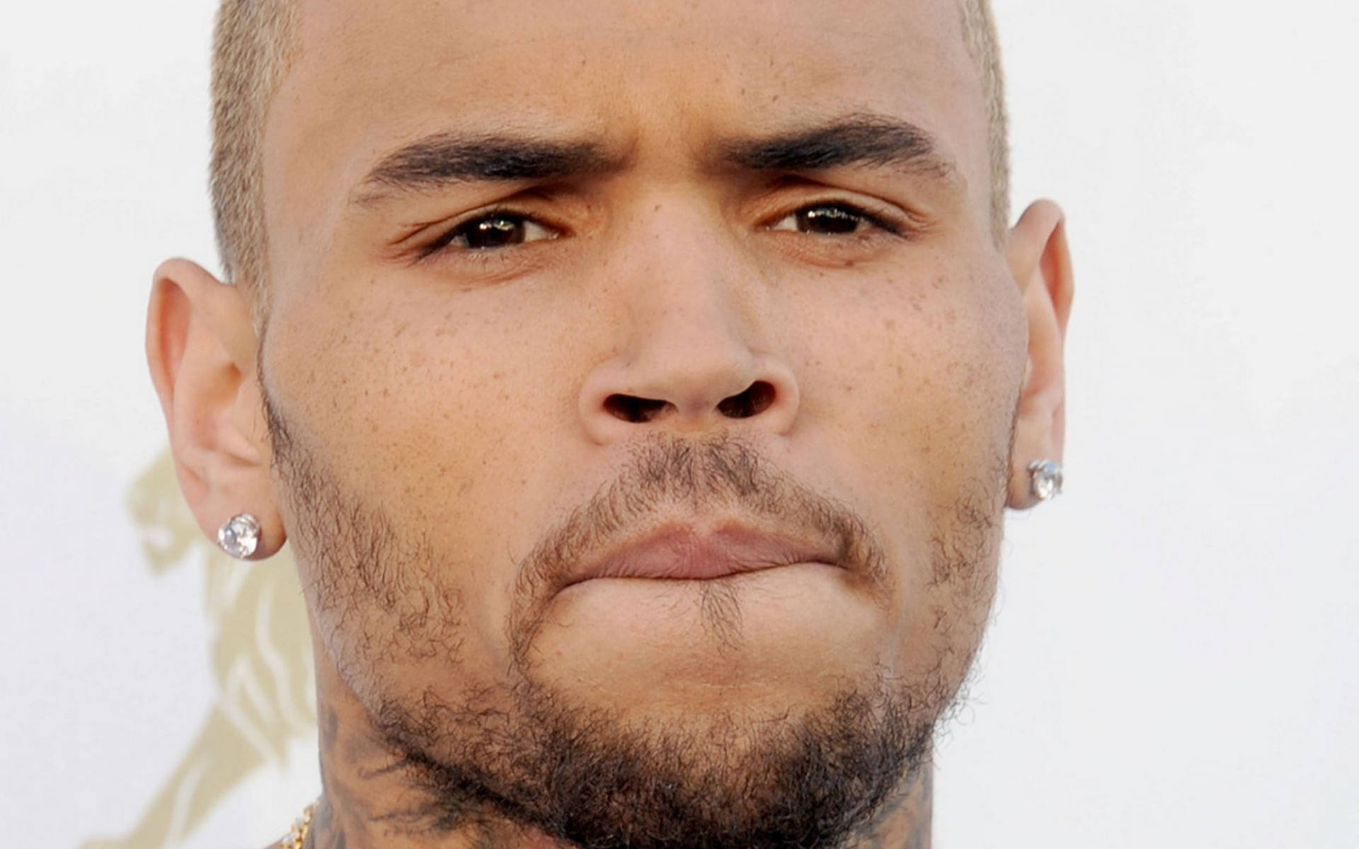 克里斯·布朗 近距離特寫 壁紙 — Chris Brown 戴鑽石耳環、表情嚴肅嘅特寫肖像，背景係明亮嘅白色。