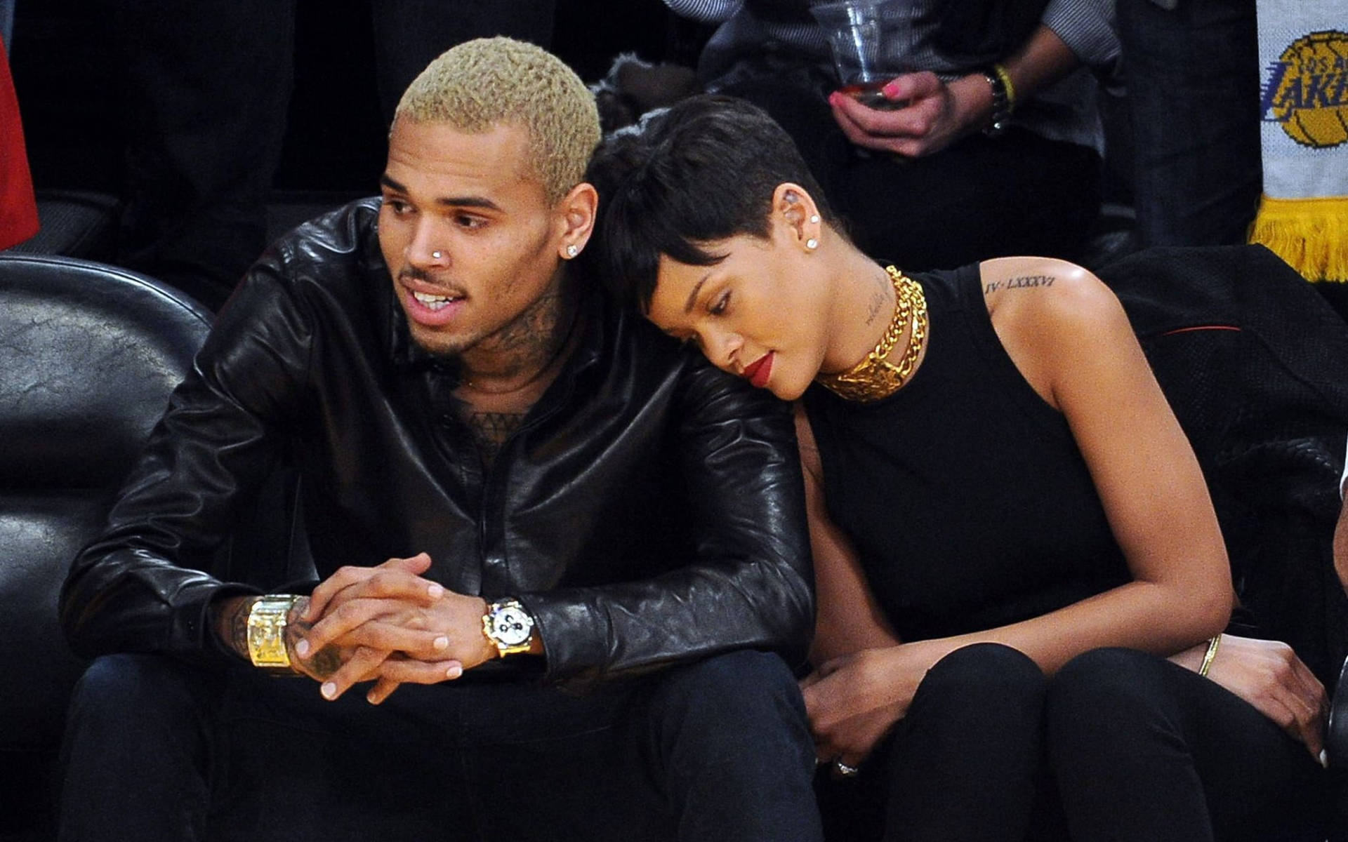 克里斯·布朗與蕾哈娜 壁紙 — Chris Brown 和 Rihanna 在籃球賽中緊貼著坐在黑色皮革座椅上，她的頭靠在他的肩膀上。