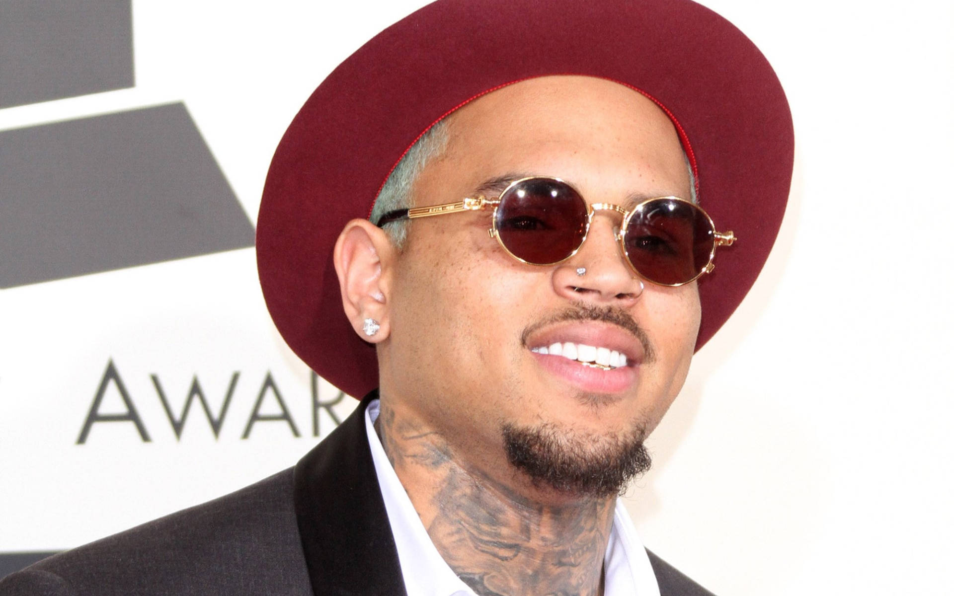 克里斯·布朗頒獎典禮 壁紙 — Chris Brown 在格林美獎上自信微笑，戴著栗色帽子、金色邊框太陽眼鏡和黑色西裝。