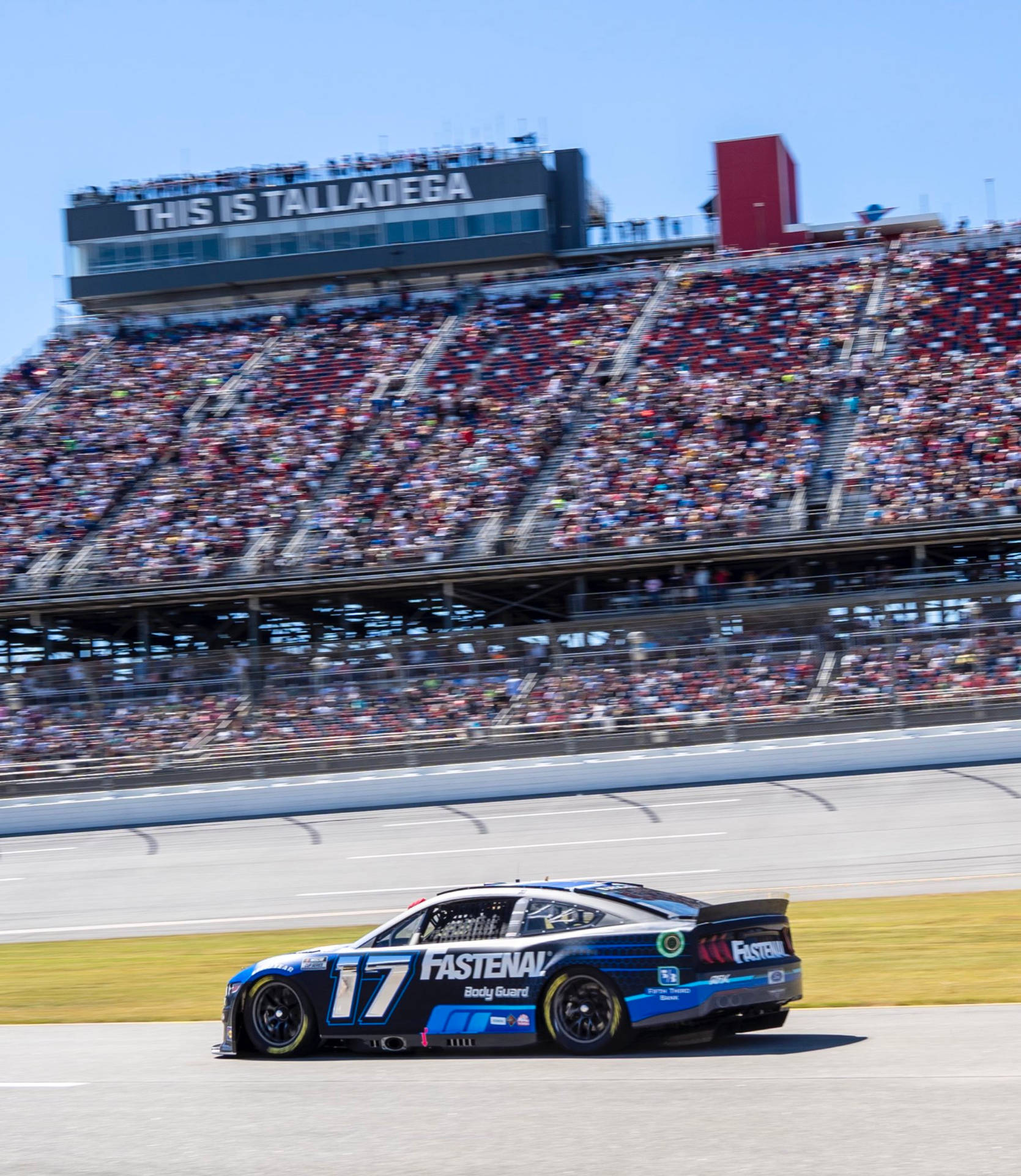 藍黑相間的NASCAR賽車在賽道上高速行駛，背景是歡呼的人群。