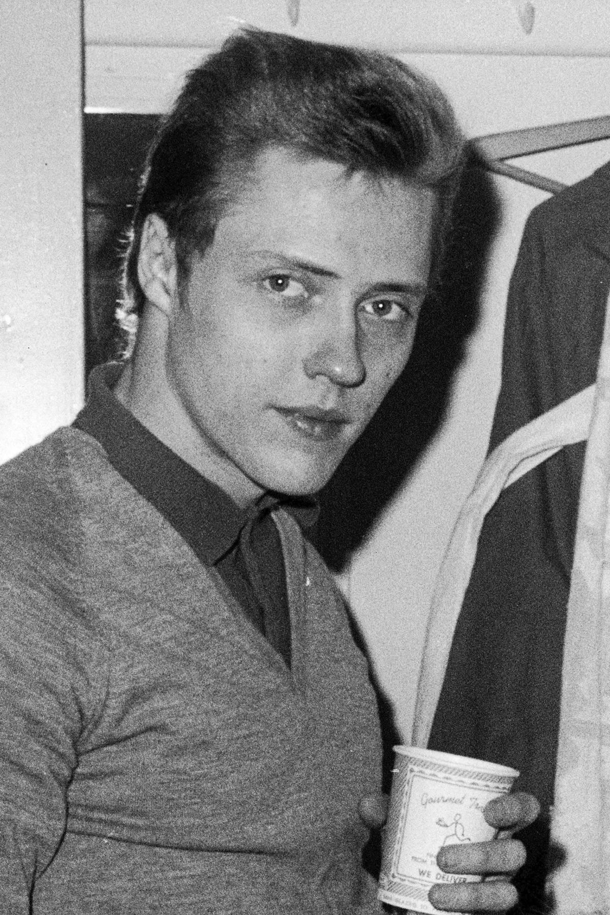 身穿1960年代服裝的年輕男子，在自然隨性的黑白照片中手持咖啡杯。