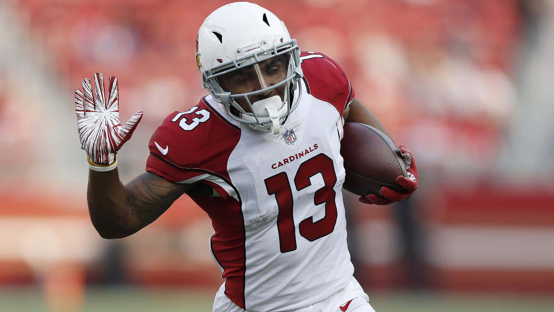 身穿 Cardinals 球衣的足球員持球奔跑並揮手。