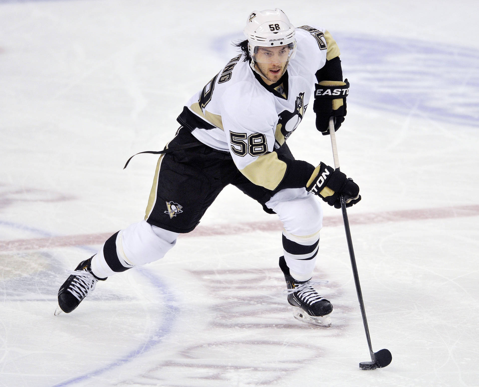 克里絲·萊唐 NHL 比賽 壁紙 — 一名身穿黑金色球衣的冰球運動員手持球桿在冰上激烈滑行。