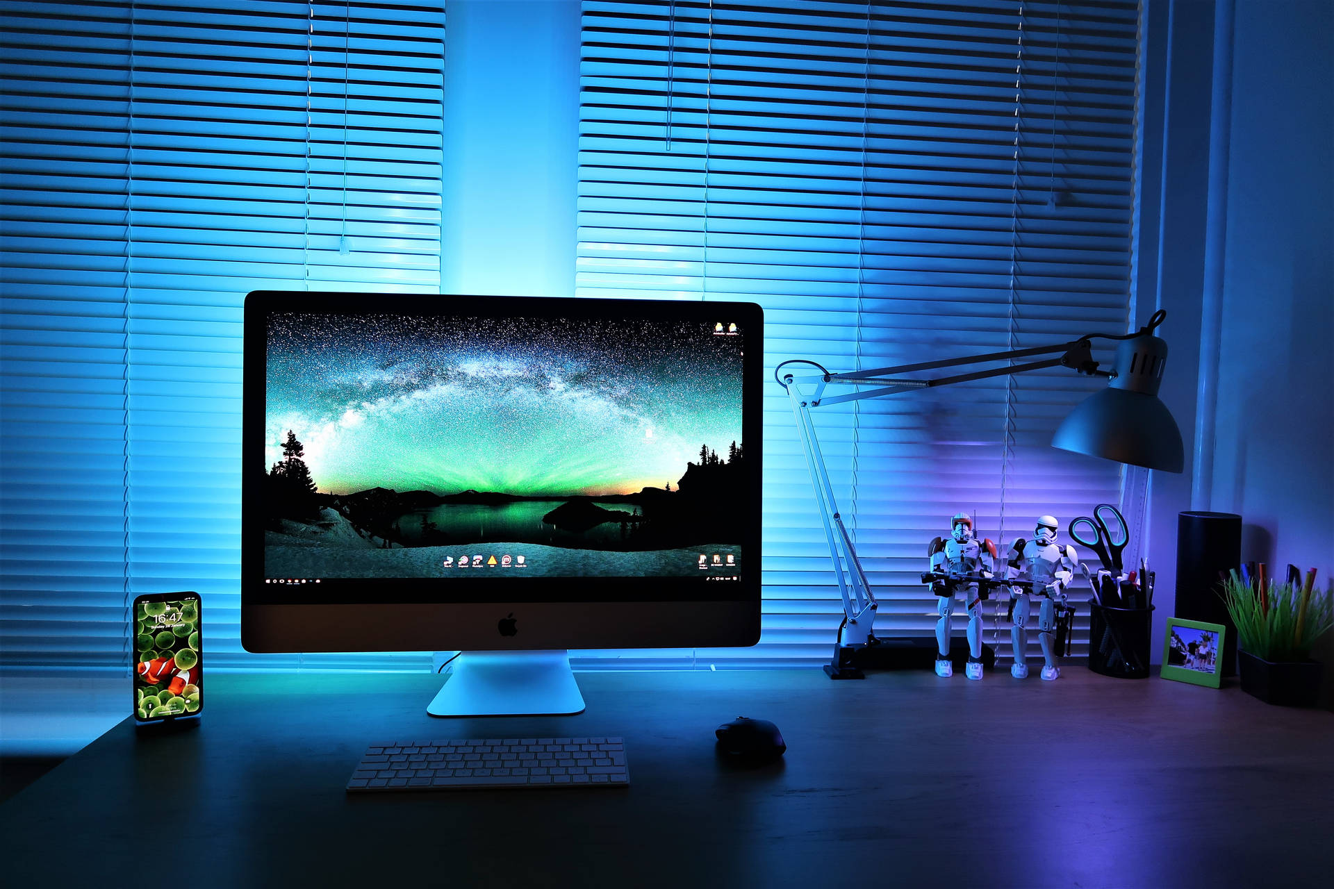 一張發藍光的桌子，上面有顯示極光壁紙的 iMac 和暴風兵人偶。