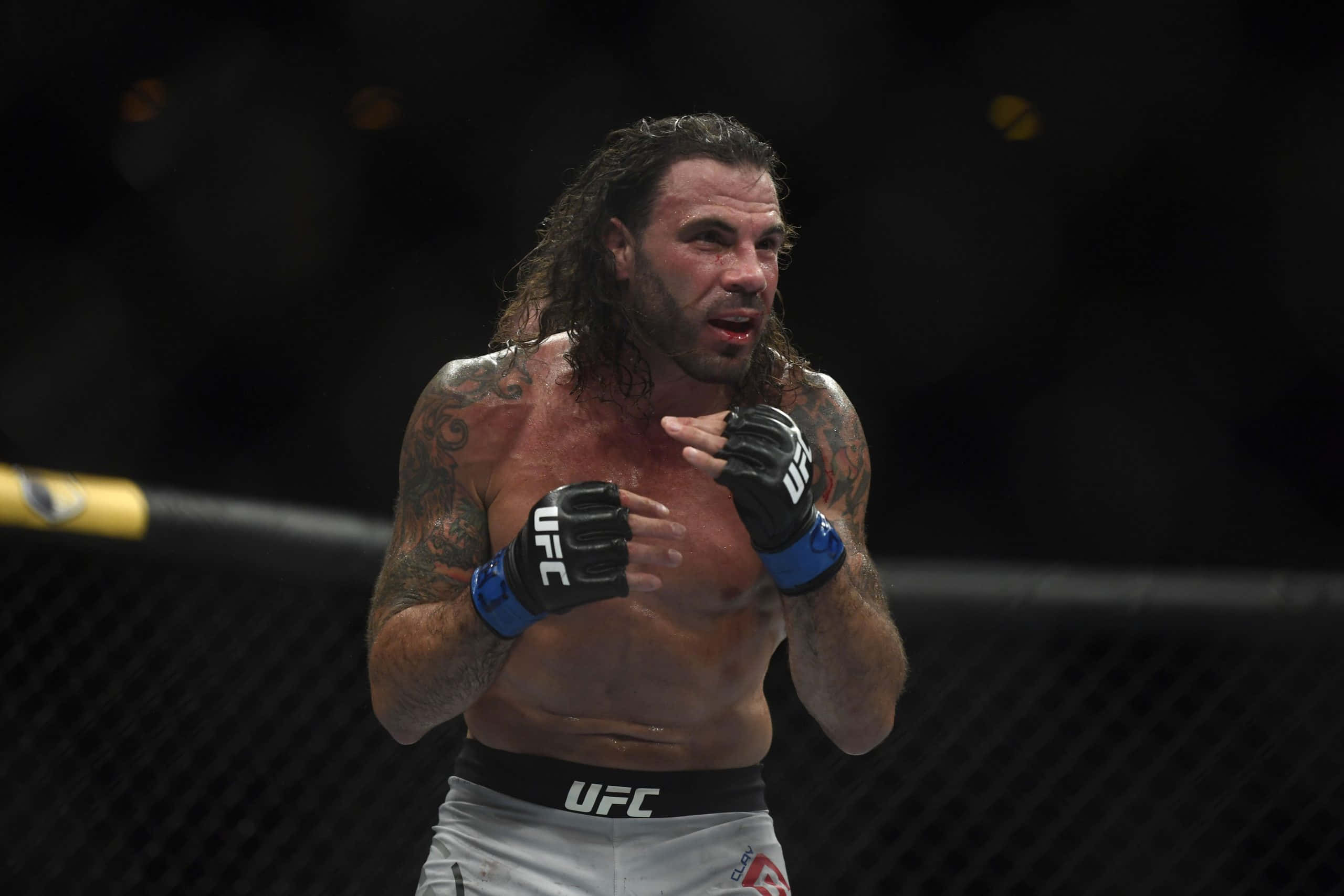 克雷頓·吉達於UFC 237 2019對戰BJ·彭恩 壁紙 — 一位有紋身、長髮的UFC拳手在明亮的八角籠內慶祝。