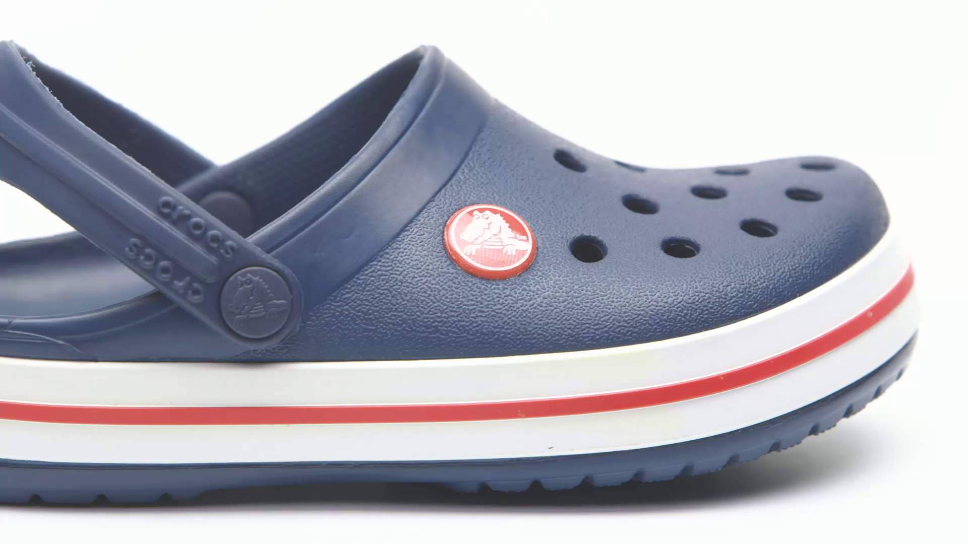 兒童 Crocs 沙灘鞋 壁紙 — 海軍藍色 Crocs 木屐的特寫，鞋底有紅白條紋，背景為白色。