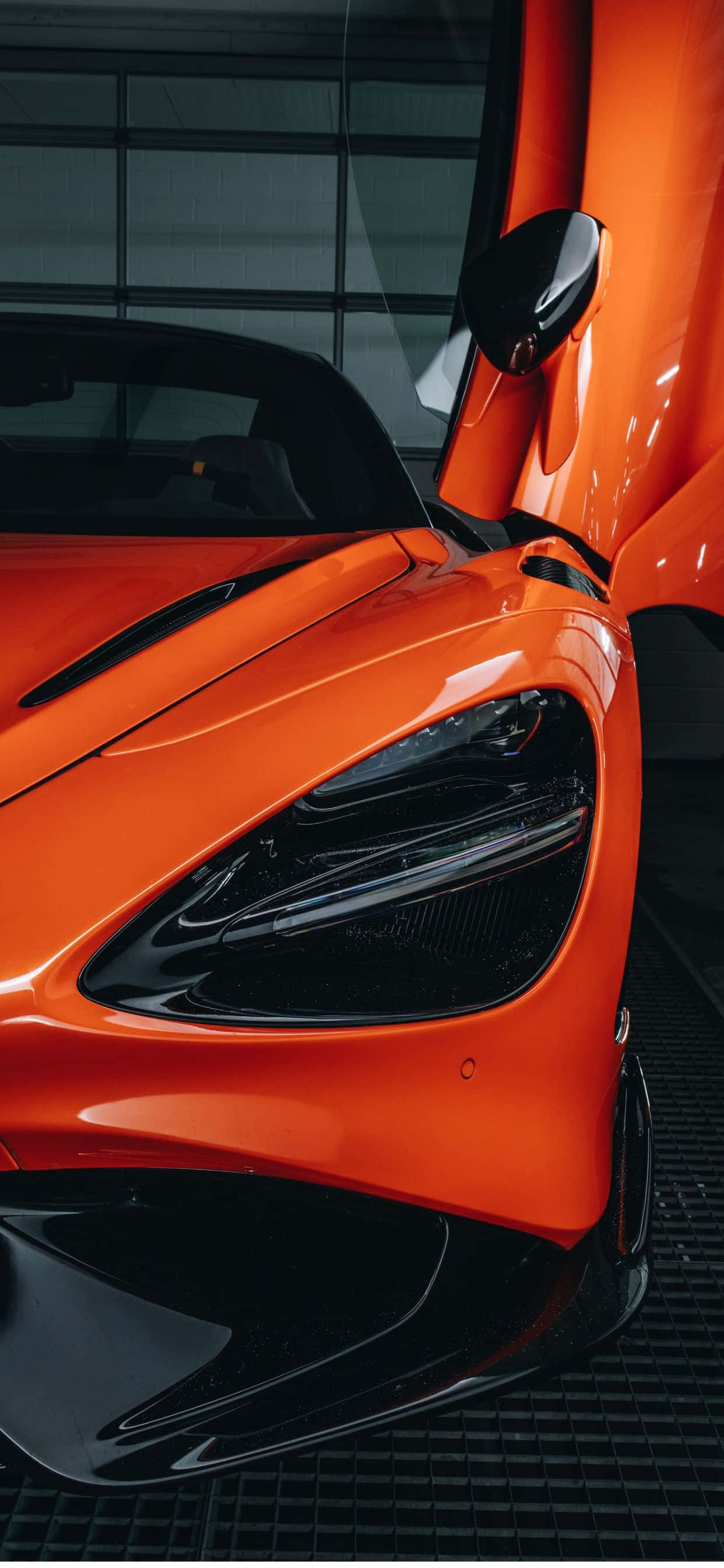 入手頂級組合：iPhone Xs Max 與 McLaren 720s 壁紙 — 一輛充滿活力的橙色McLaren跑車的特寫，車門打開，在現代車庫中展示流暢的空氣動力學曲線和光澤表面。
