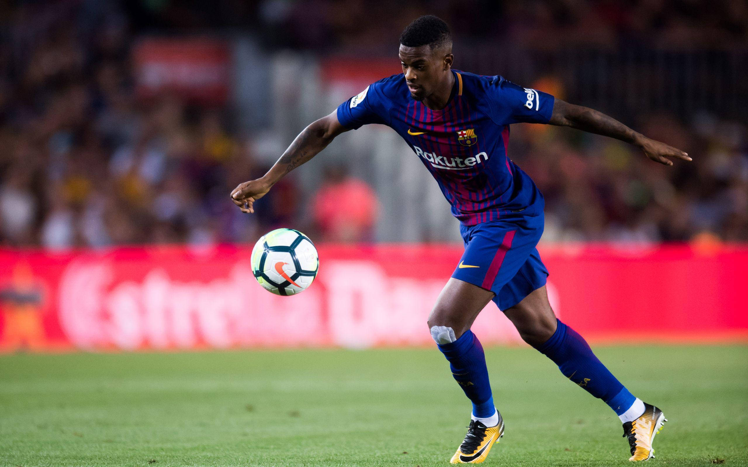 內爾森·塞梅多即將射門 壁紙 — 一名身穿藍色條紋球衣的足球運動員在體育場燈光下，於充滿活力的綠色球場上，在跨步中控制著一個白藍相間的球。