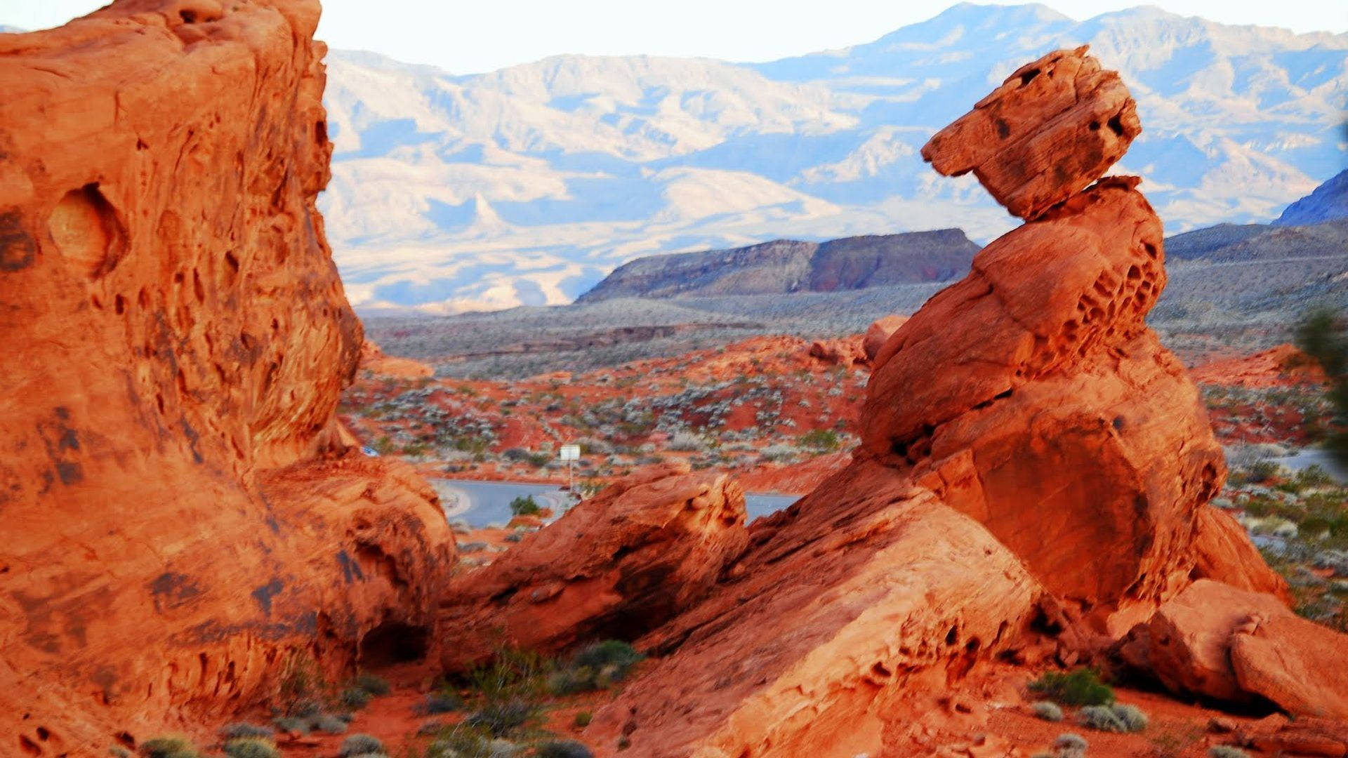 在沙漠中平衡的紅色岩石結構，背景有遠山和一個小湖。