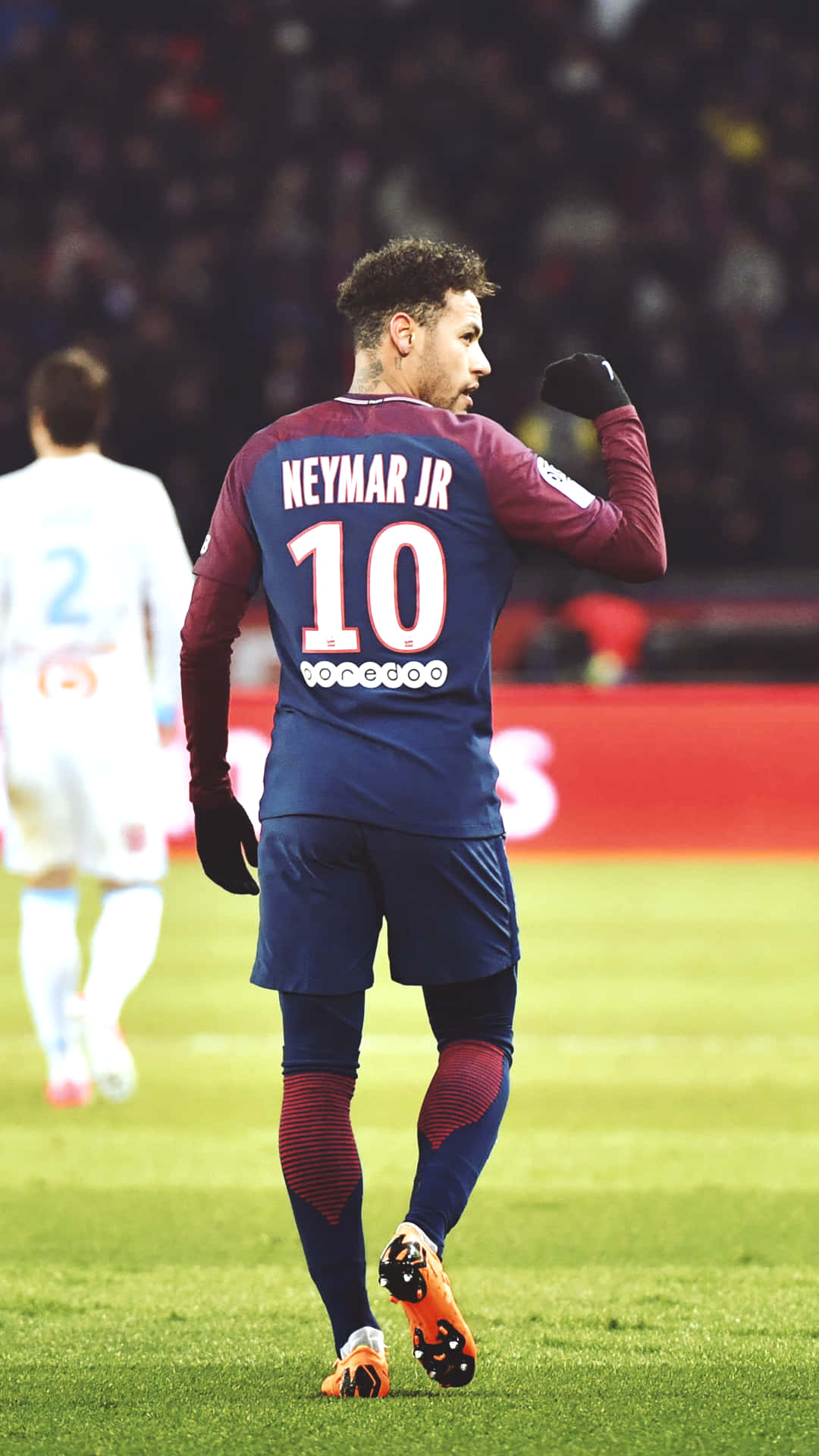 足球員尼馬（Neymar Jr）在燈光明亮的體育場上身穿藍色和栗色球衣慶祝。