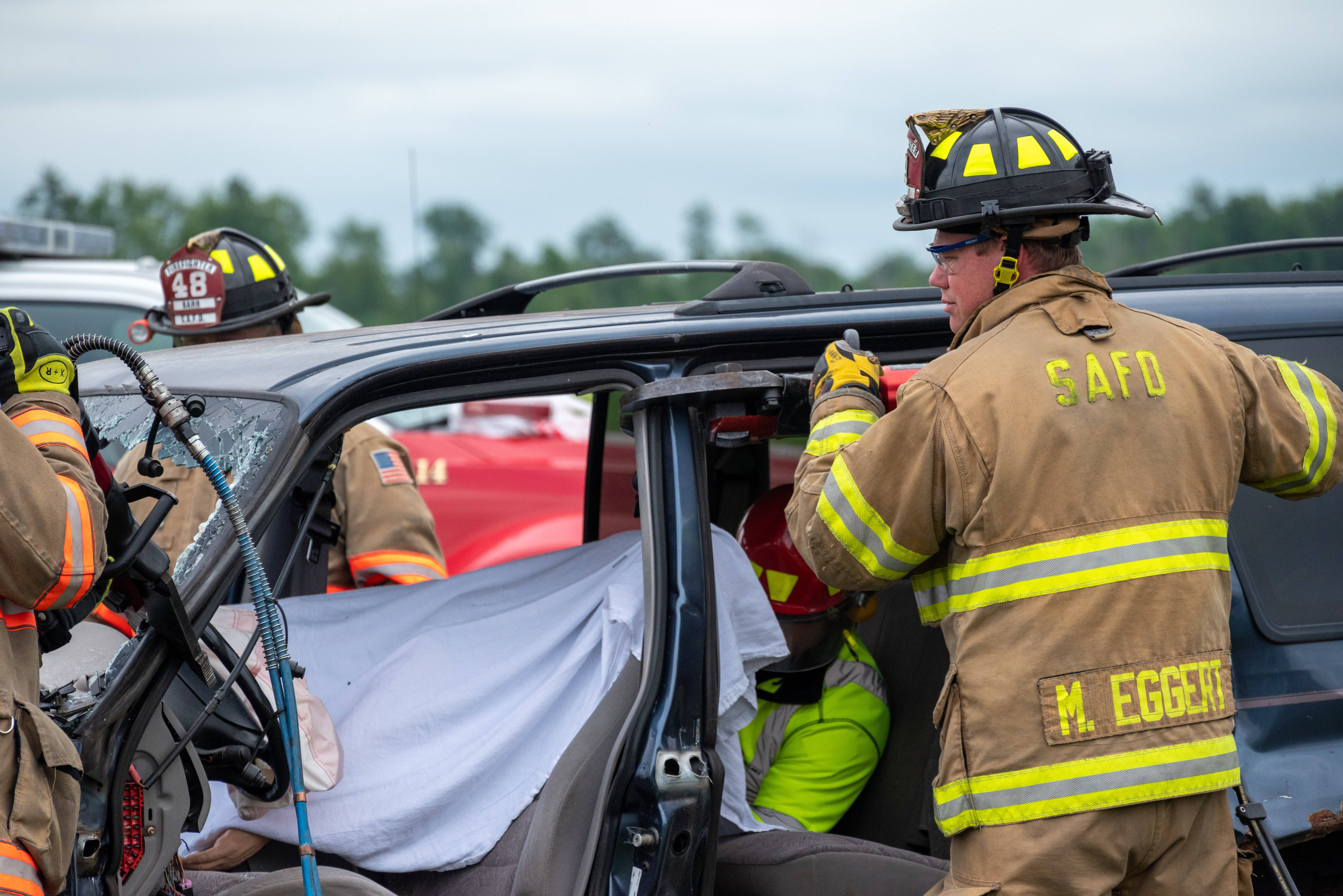 car crash 桌布 壁紙 — 全副裝備的消防員在日間救援行動中使用液壓工具從一輛被壓碎的SUV中救出一人。