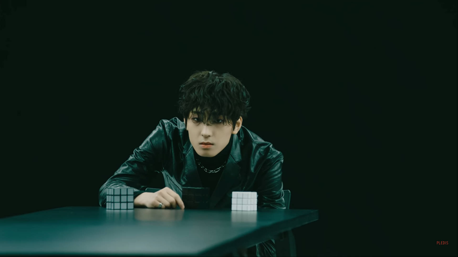 全圓佑《HIT》MV 壁紙 — 一名身穿黑色皮褸的年輕男子，在陰暗的綠色燈光下，俯身於一張放有兩個扭計骰的深色桌子上。