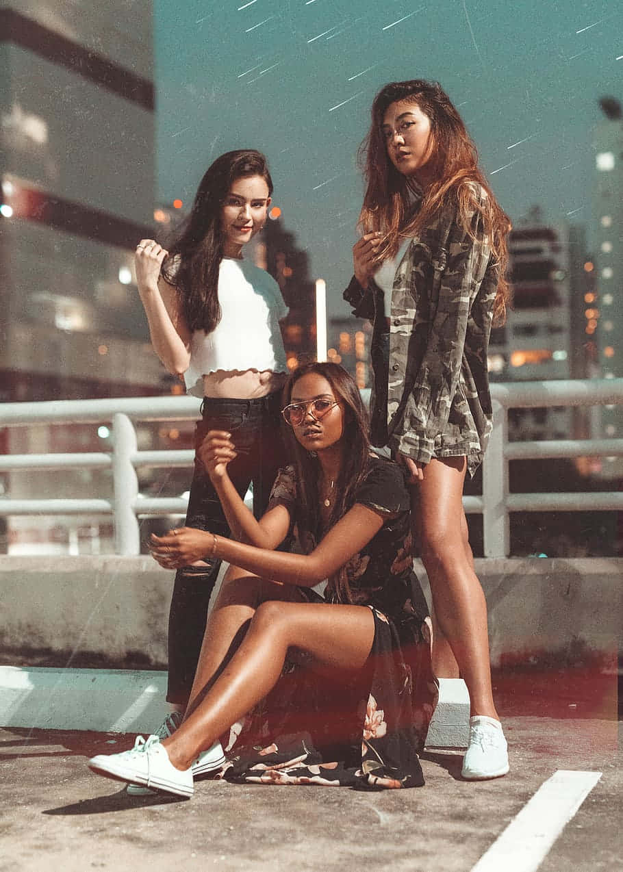 三位女性在夜晚的屋頂上，背後是城市燈光。