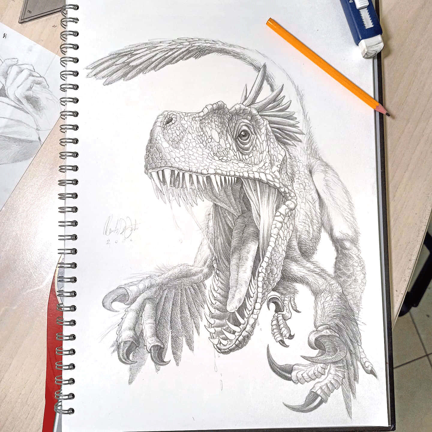 全彩恐龍繪畫 壁紙 — 一幅詳細的鉛筆素描，描繪一隻兇猛、有羽毛的恐龍，擁有鋒利的牙齒和爪子，畫在素描本中，旁邊有一支橙色鉛筆。