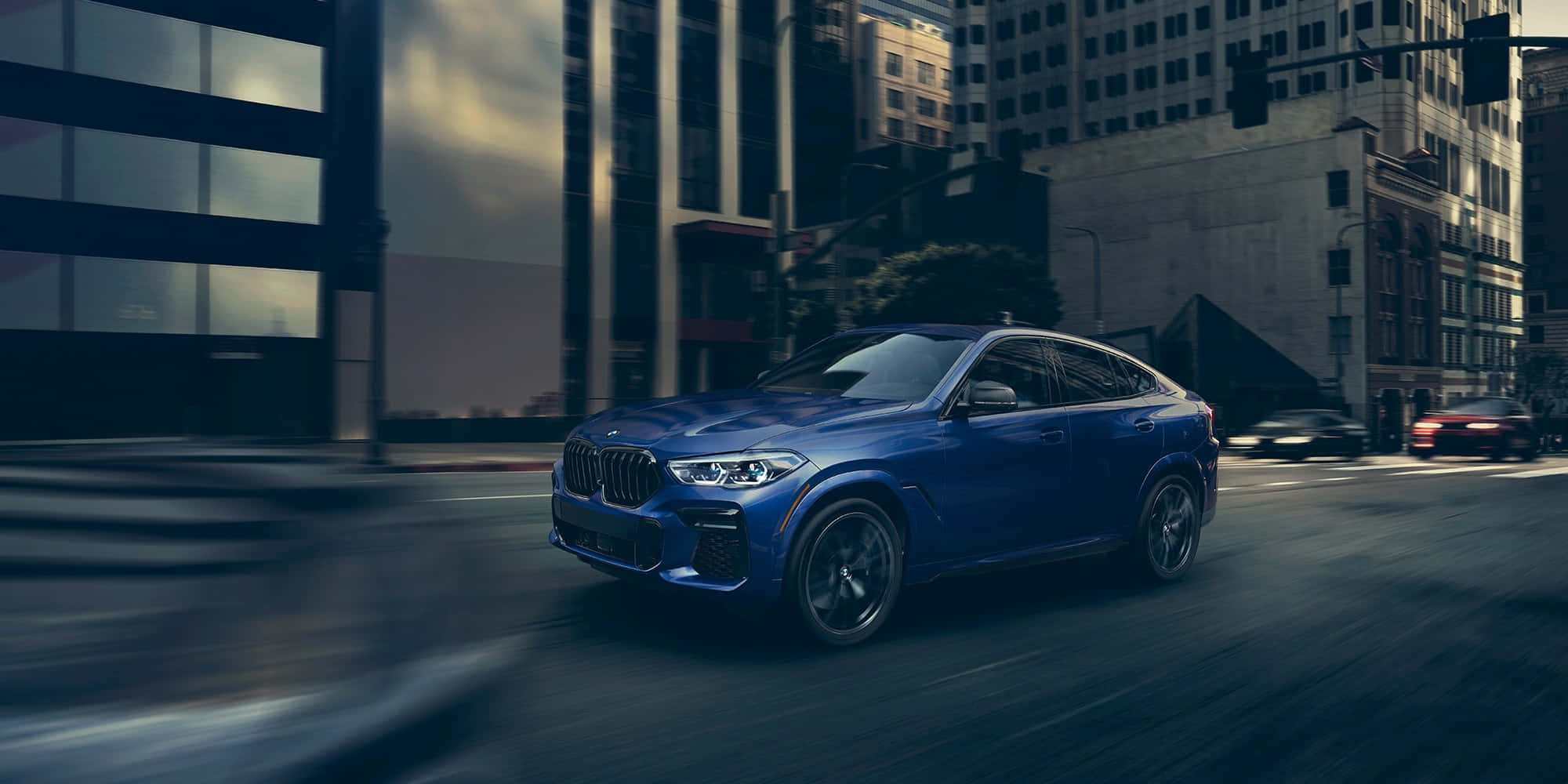 全新BMW X6 M 壁紙 — 一輛時尚的藍色寶馬X6 Coupe在街道上飛馳，背景有高樓大廈和動態模糊效果。