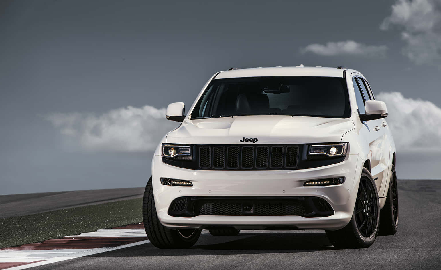 多雲天空下，賽道上帶有紅色和白色路緣石的白色Jeep SUV。