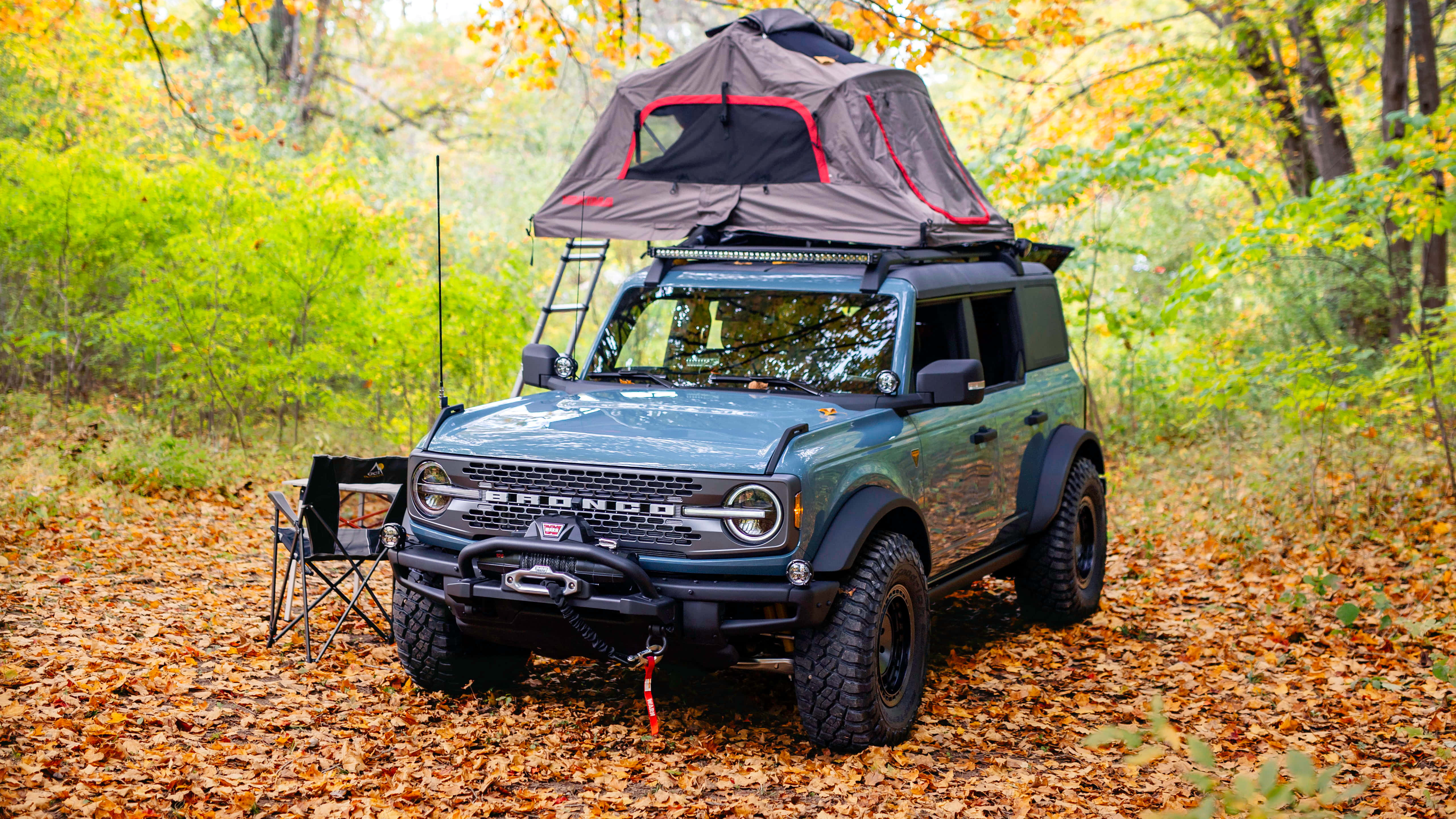 全新福特Bronco，經典藍色再現 壁紙 — 一輛綠色福特Bronco配備車頂帳篷，停泊在鋪滿金色秋葉的森林中。