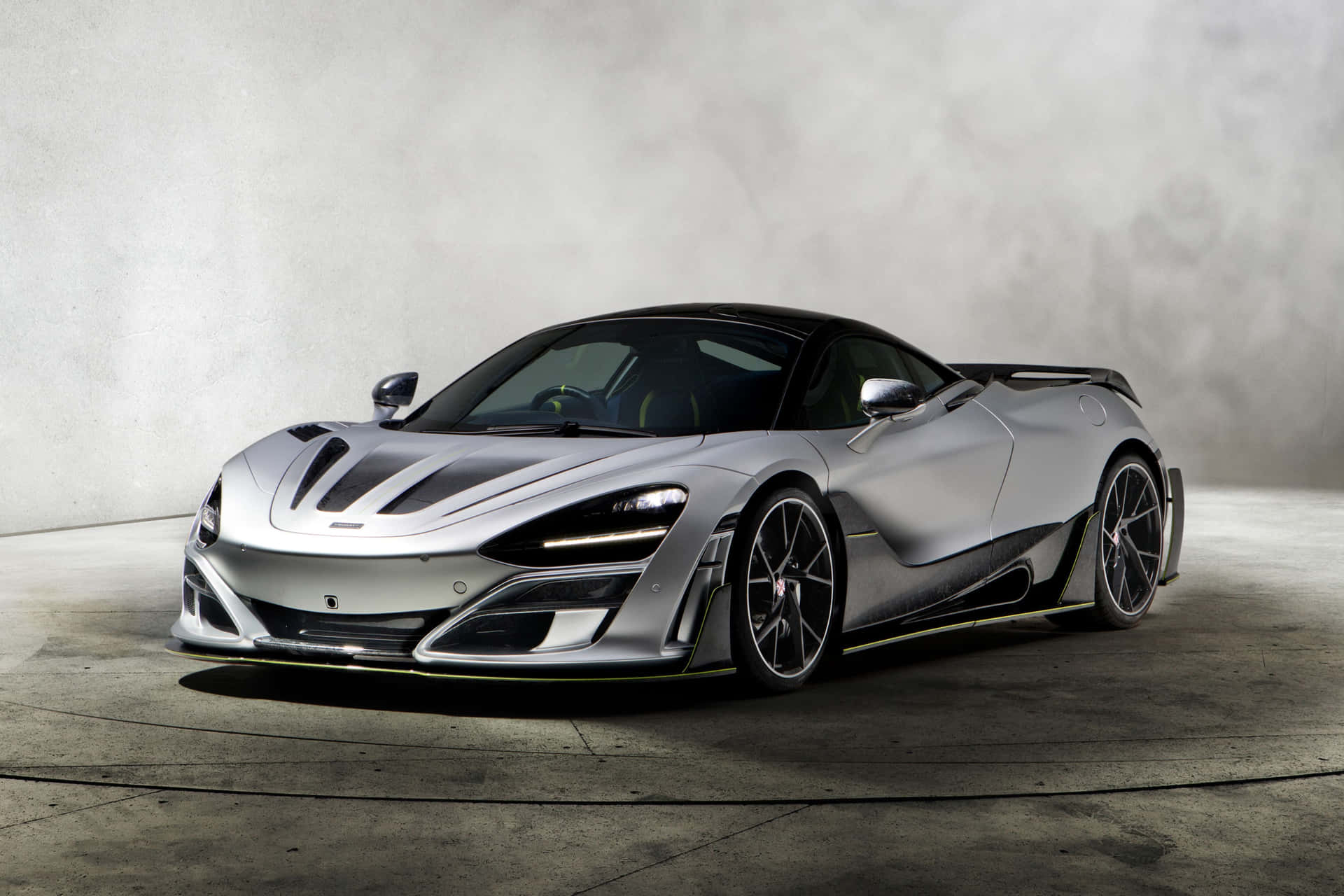 在混凝土工作室中，帶有黑色和黃色點綴的銀色McLaren超級跑車。