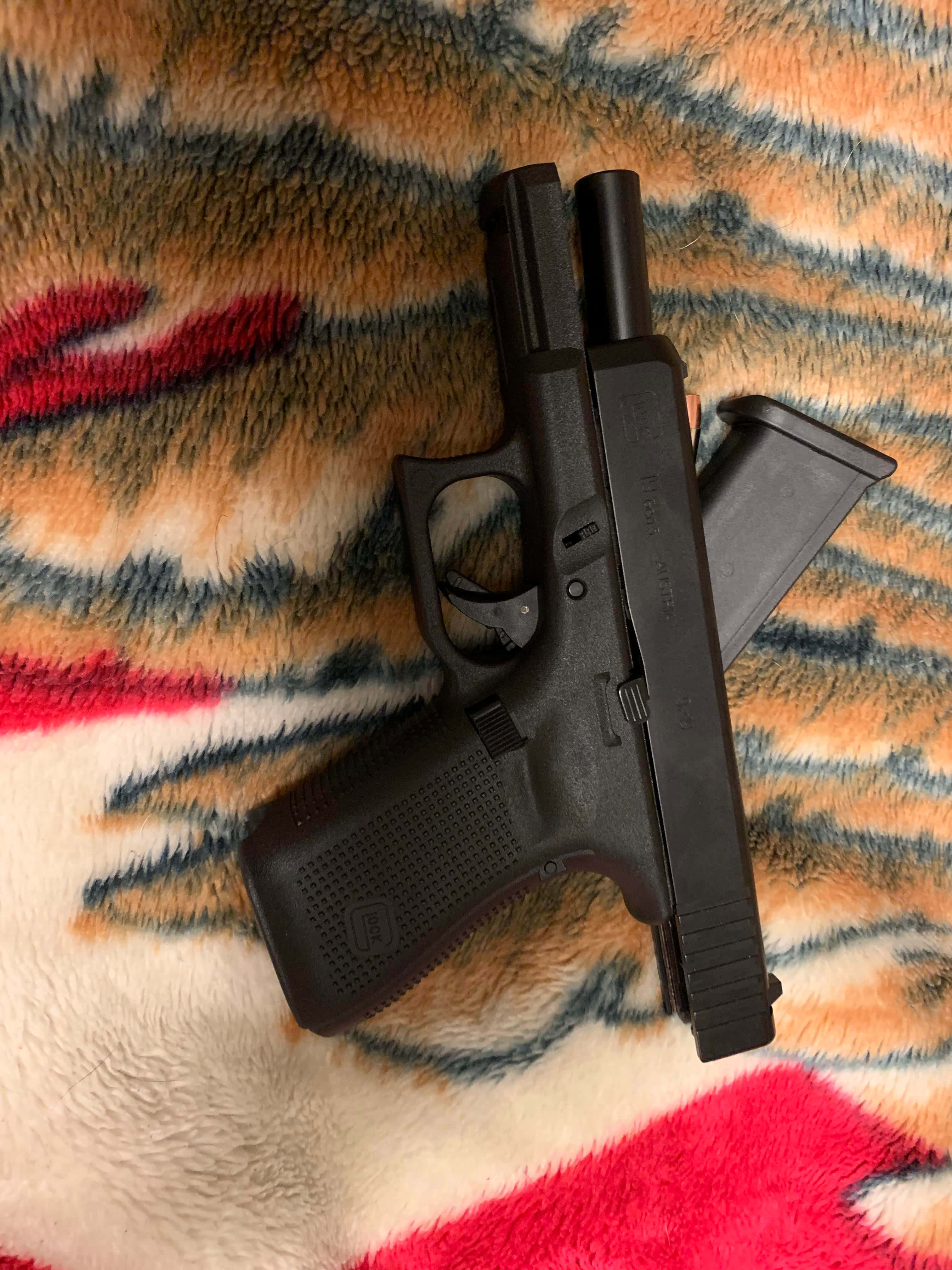 全方位手槍之選 —— Glock 19 壁紙 — 一支黑色手槍和彈匣放在一條色彩繽紛、毛茸茸的毯子上，毯子有橙色、紅色和藍色的圖案。