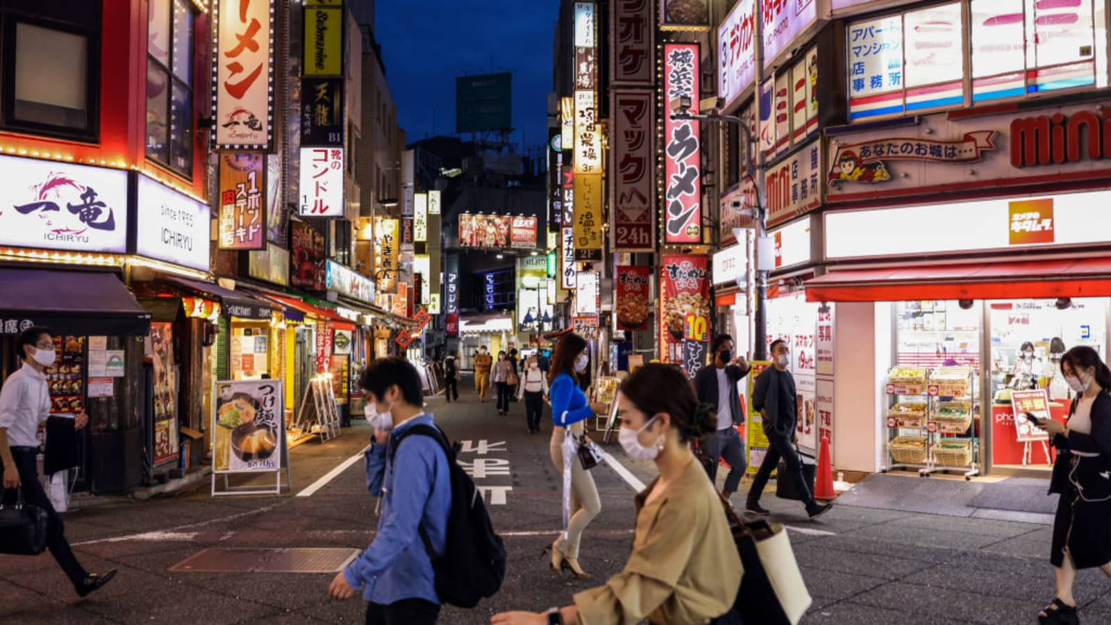 戴著口罩的人們在夜晚走過東京一條充滿活力的霓虹燈小巷，頭頂是發光的招牌。