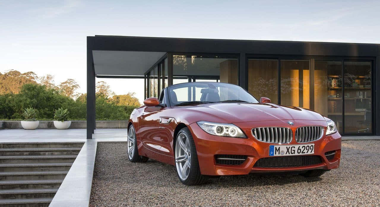 紅色BMW Z4開篷車在日落時停泊在現代玻璃屋前。