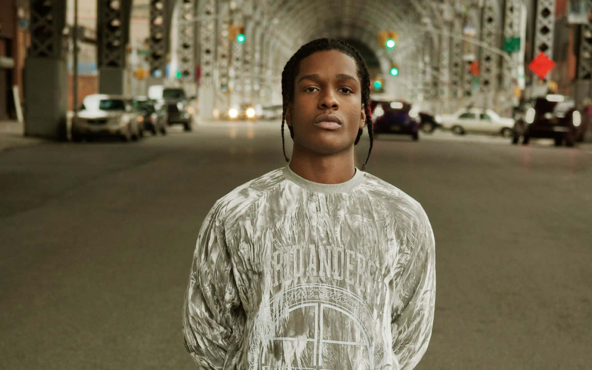 全球嘻哈藝術家 ASAP Rocky 壁紙 — 一名辮子髮型的年輕男子自信地站在橋下的城市街道中央，背景有汽車和交通燈。