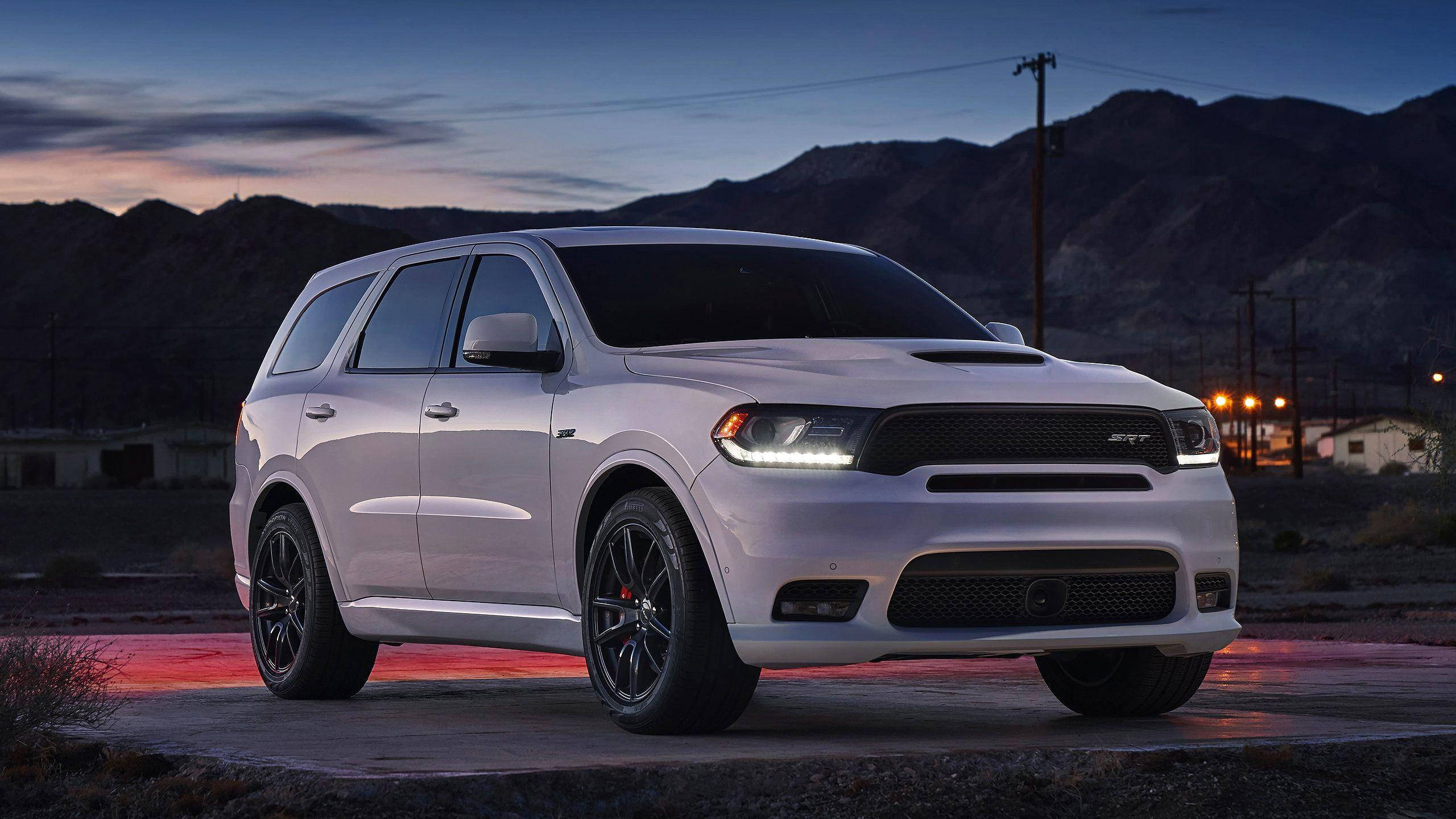 全白Durango車款 壁紙 — 一輛白色Dodge Durango SRT SUV，配黑色輪圈，停泊在黃昏時分的混凝土墊上，背景有山脈和遠處燈光。