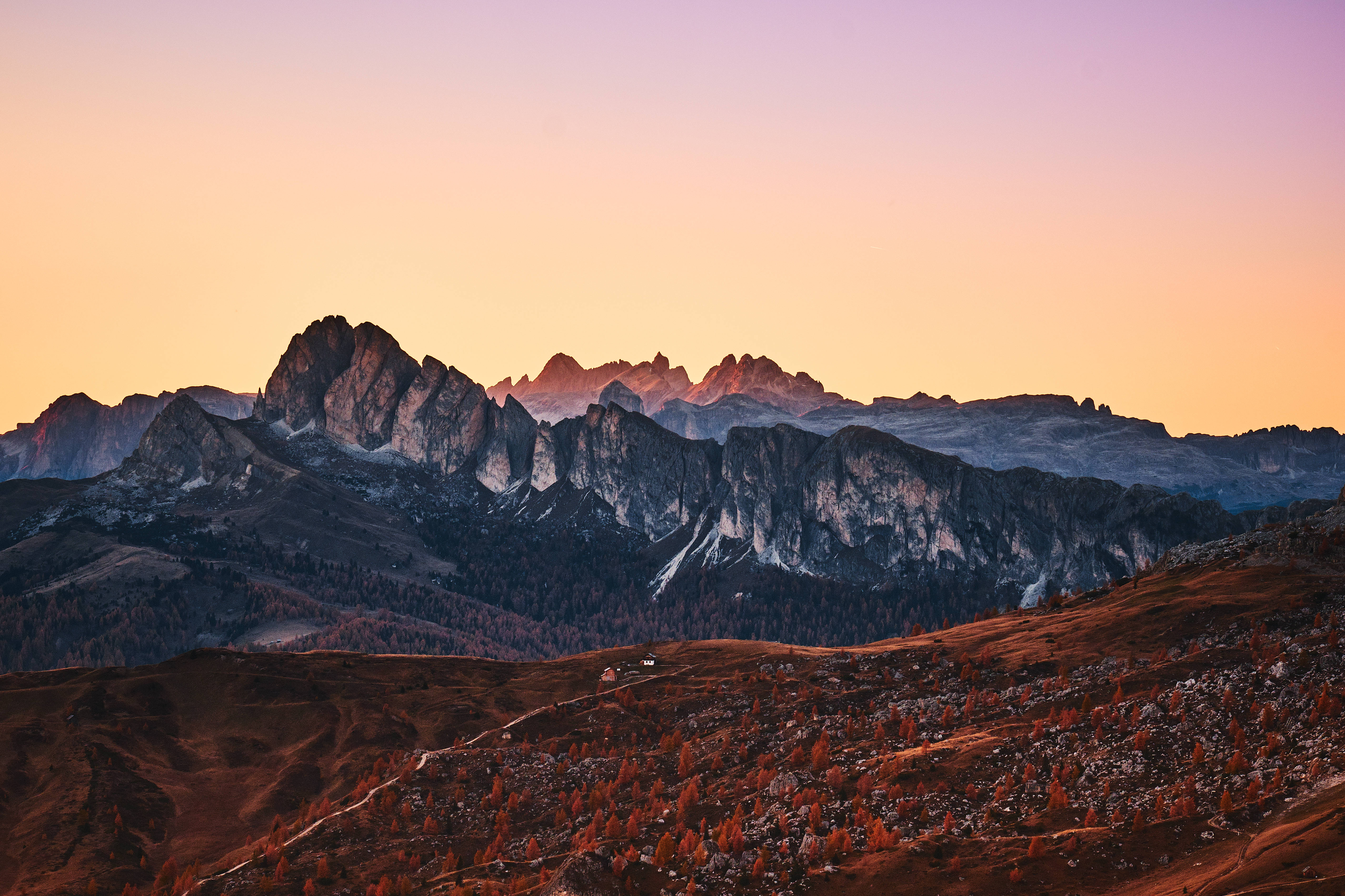 全螢幕HD山峽風景 壁紙 — 夕陽將崎嶇的山峰染成溫暖的金色和紫色，秋天的樹木在下方閃耀。