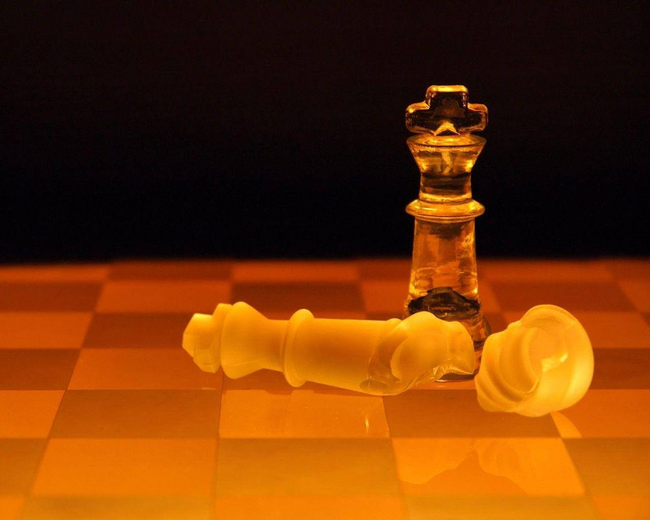 全螢幕HD棋子 壁紙 — 一隻倒下的白色國際象棋兵躺在一個站立的琥珀色國王面前，棋盤在溫暖的燈光下，背景黑暗。