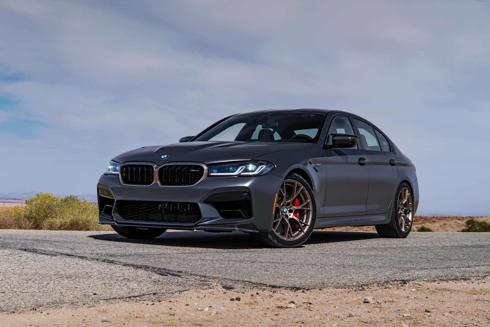 啞光灰色BMW M5運動轎車配備青銅輪圈，停在日落時分的沙漠路上。