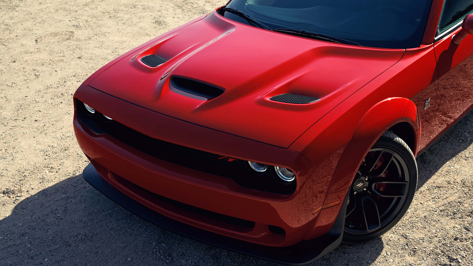 陽光下碎石地上的紅色Dodge Challenger RT跑車。