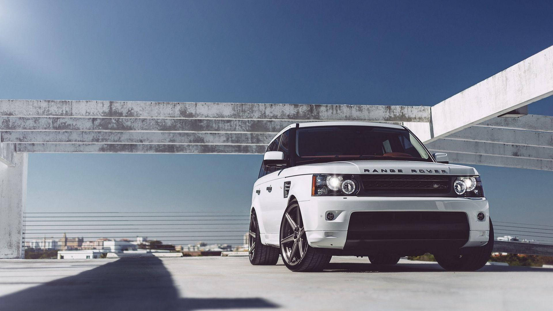 全高清白色路虎SUV 壁紙 — 一輛純白色的Range Rover SUV在晴朗的藍天下，大膽地停在風化的混凝土天橋下。