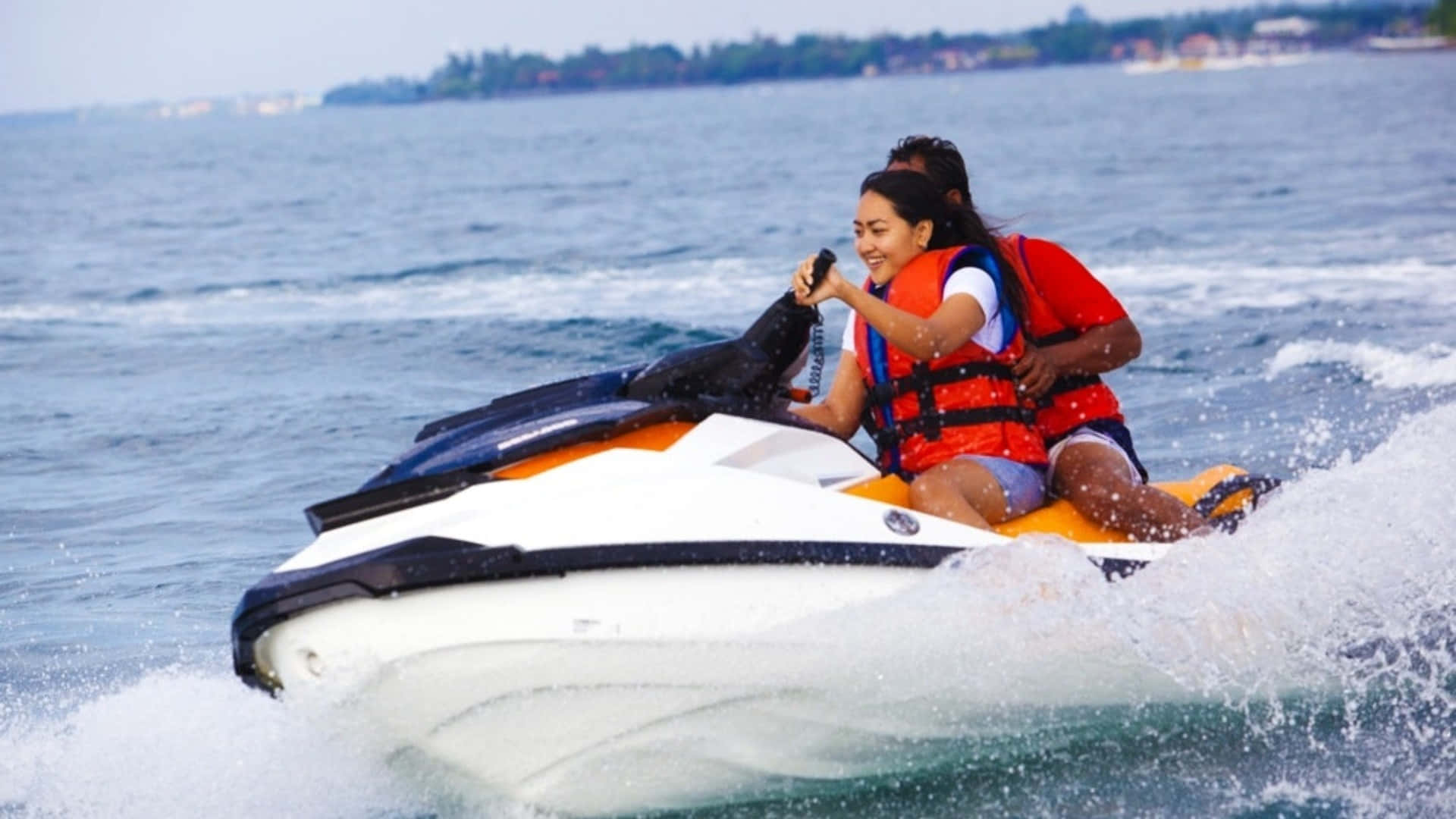 Beach Water Sports 桌布 壁紙 — 兩人穿著救生衣，騎著白色橙色水上電單車穿過藍色海水，激起水花。