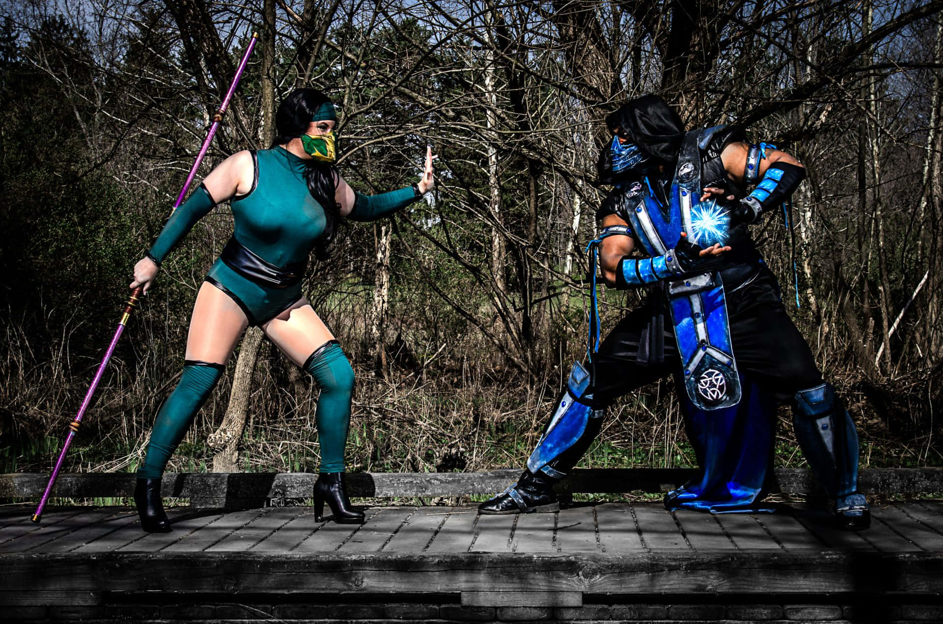 Mortal Kombat Cosplays 桌布 壁紙 — 兩位Cosplayer穿著真人快打服裝在光禿禿森林的木橋上衝突，一人揮舞著法杖，另一人發出藍色光芒的能量。