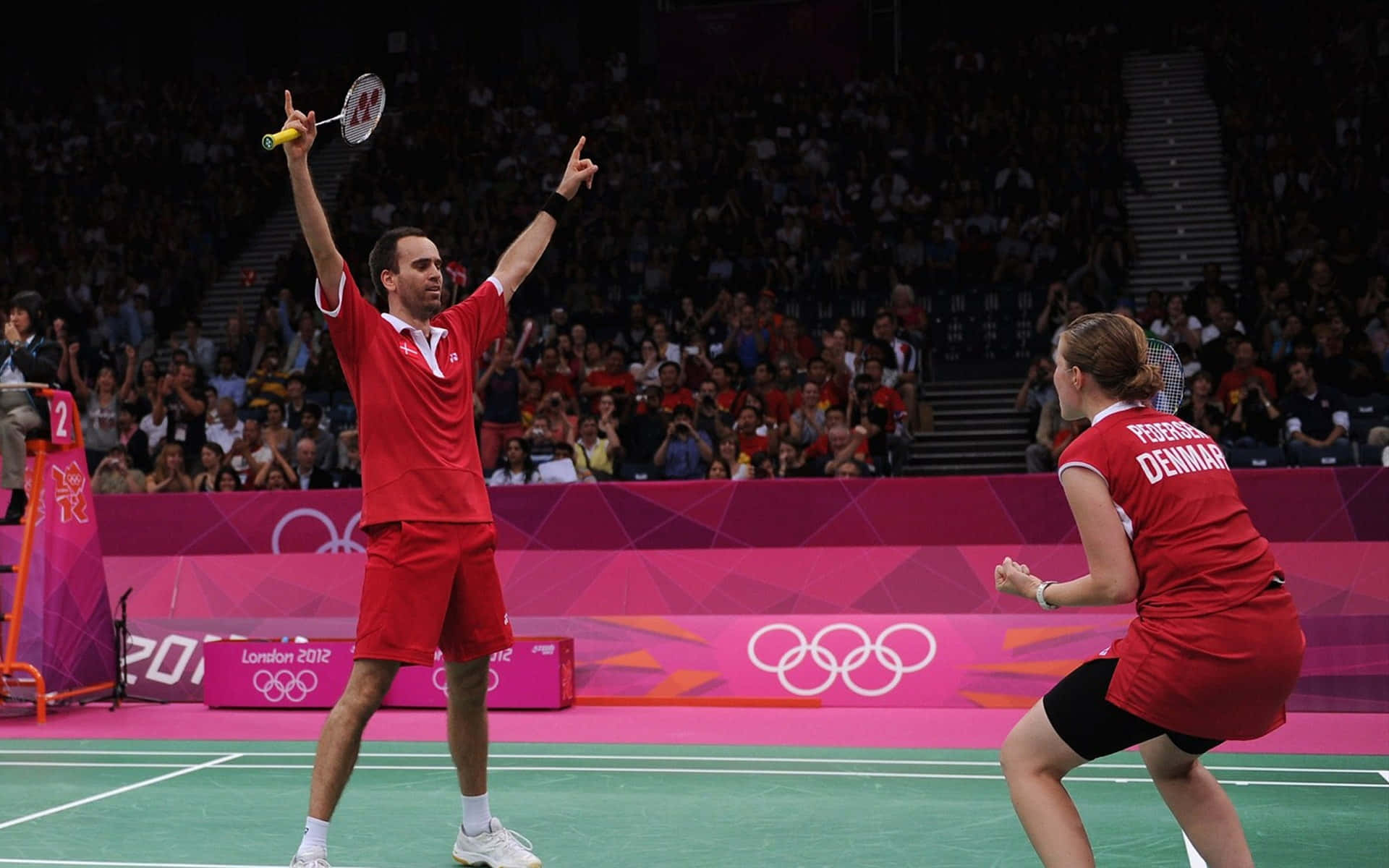Badminton 桌布 壁紙 — 兩位丹麥羽毛球選手在燈光明亮的奧運場館中，在歡呼的人群中慶祝得分勝利。
