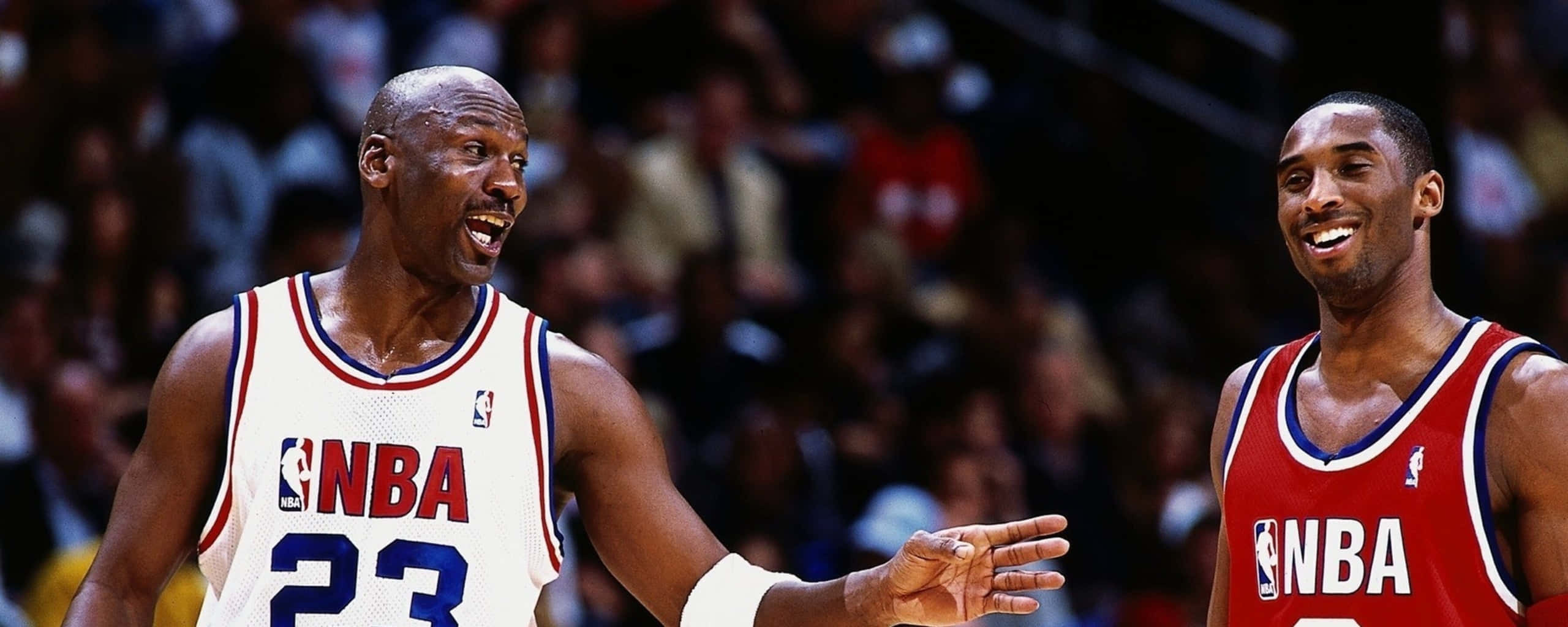 兩位傳奇：邁克爾·喬丹與科比·布萊恩特 壁紙 — 兩位身穿NBA球衣的傳奇籃球運動員在比賽中分享歡樂時刻，背景是模糊的人群。