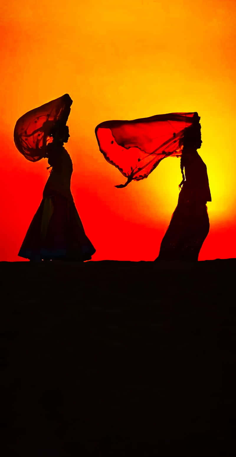 Rajasthan 桌布 壁紙 — 兩位剪影舞者披著飄逸的紅色面紗，在火紅的橙紅色日落天空下優雅舞動。