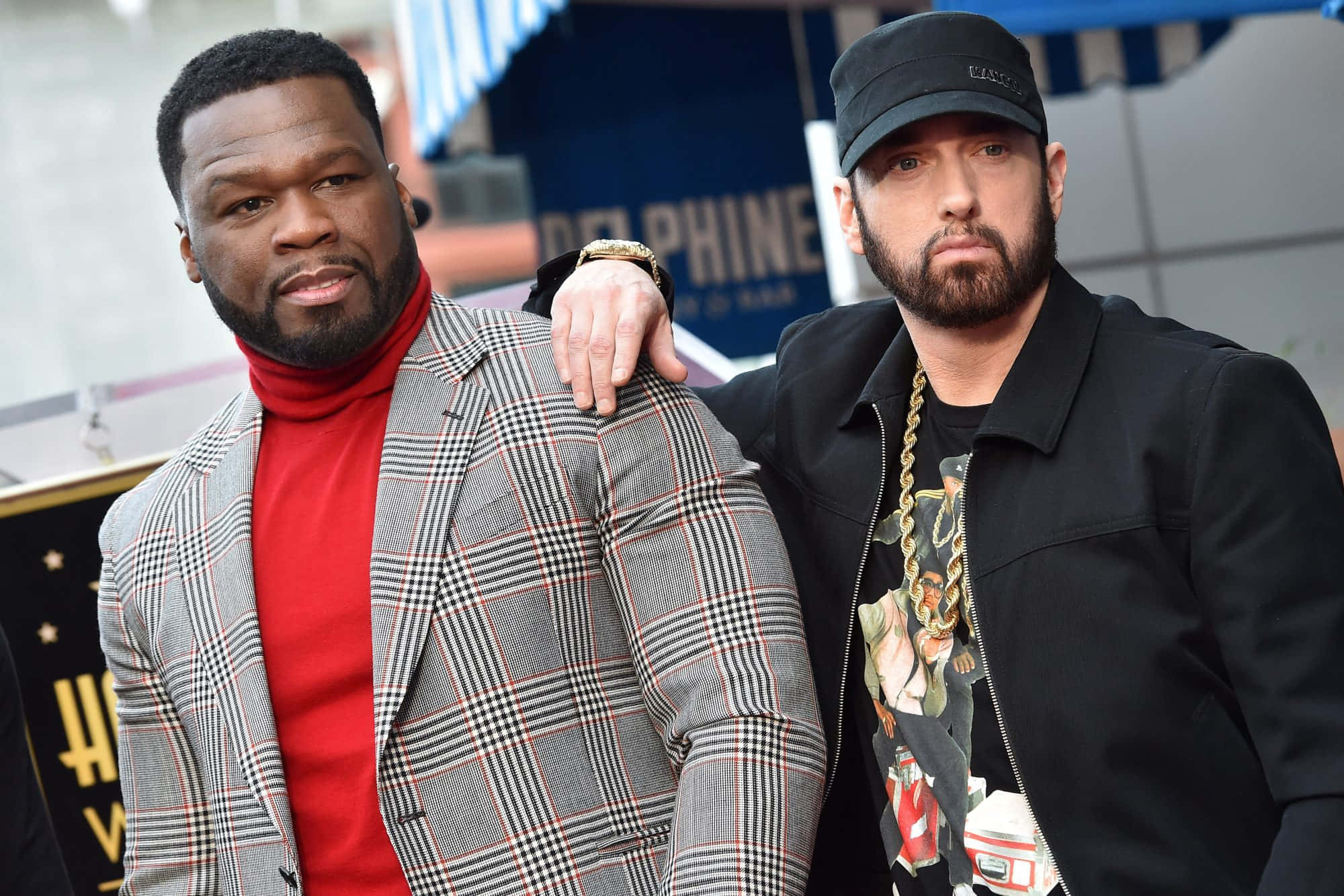 Eminem 桌布 壁紙 — 兩位嘻哈偶像在荷里活活動中自信擺姿勢，一位身穿紅色高領毛衣和格子西裝外套，另一位身穿黑色外套和金鏈。