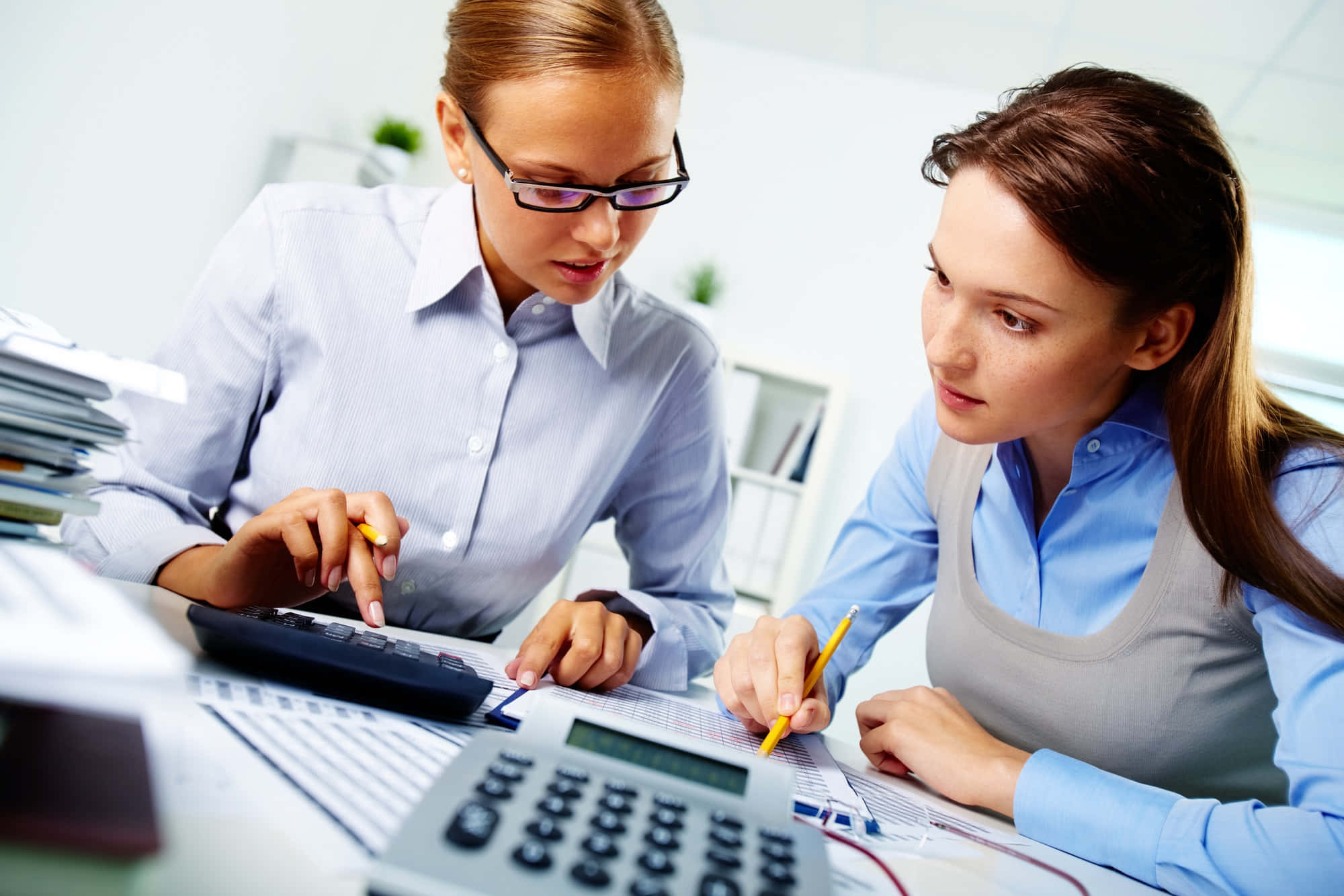 Accounting 桌布 壁紙 — 兩位女商人在明亮的辦公室環境中，專注地合作處理財務文件和計算機。