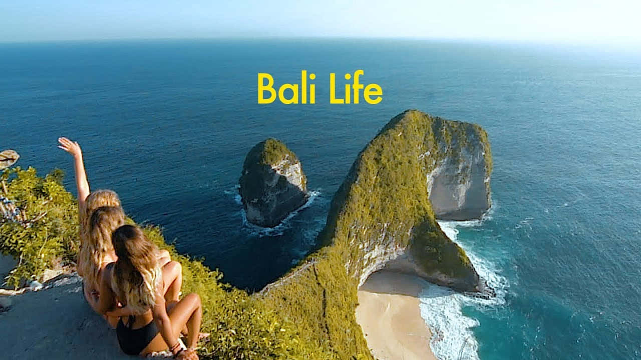 Bali Island 桌布 壁紙 — 兩位女士坐在懸崖邊，俯瞰著碧綠色的海洋和茂密的綠色海蝕柱，在明亮的日光下。