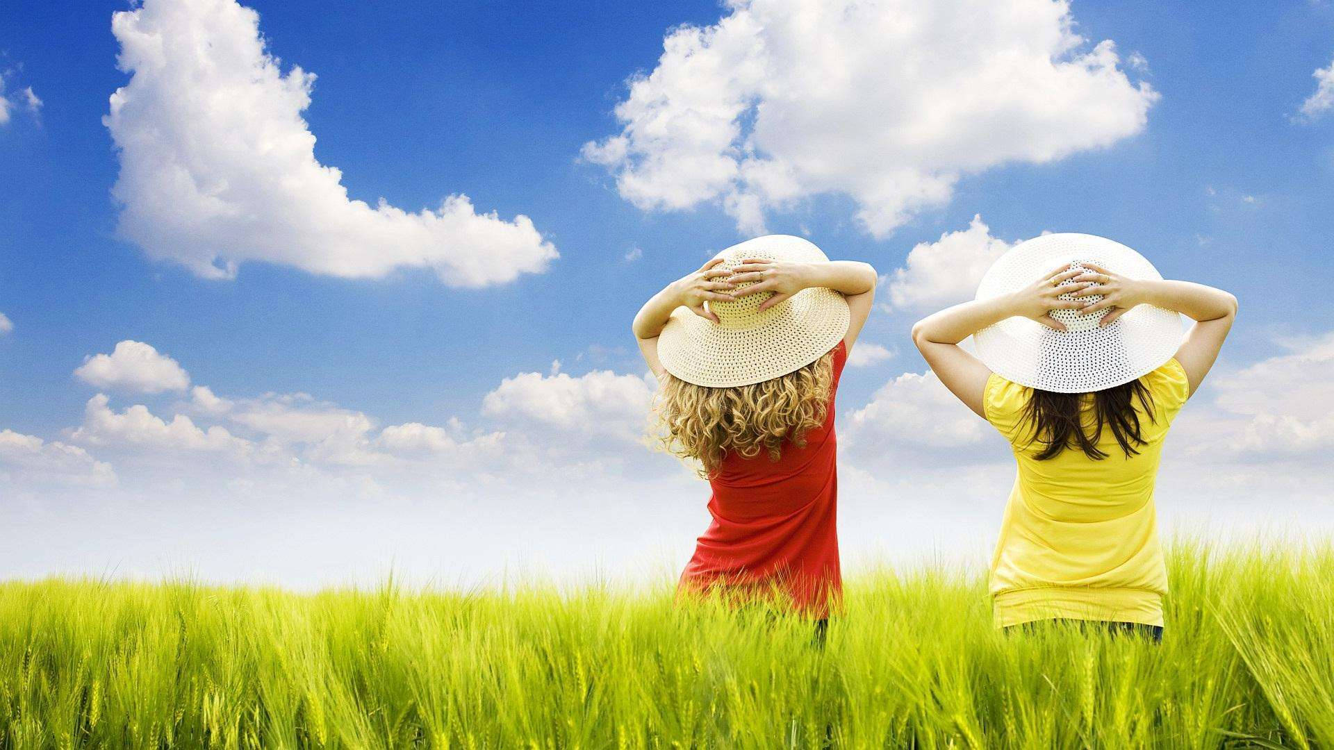 兩位戴草帽的女性在陽光明媚的綠色田野中背對背站立。