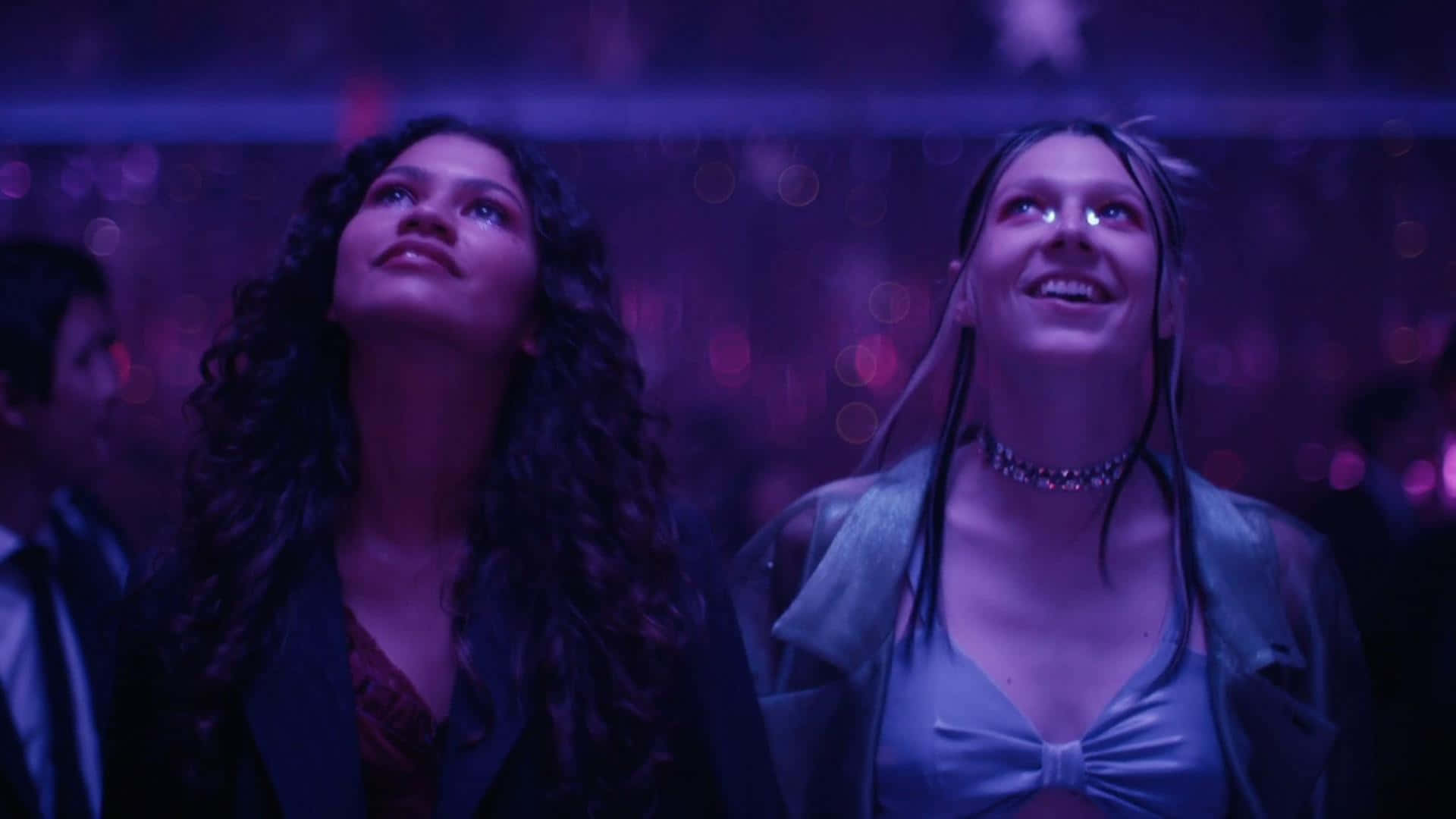 euphoria 桌布 壁紙 — 兩位女性在昏暗的紫色燈光場地中向上微笑，周圍有散景燈光閃爍。